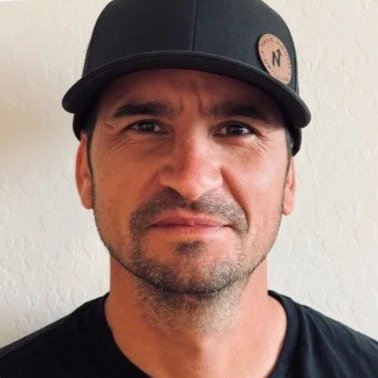A man wearing a black baseball cap with a neutral background.
