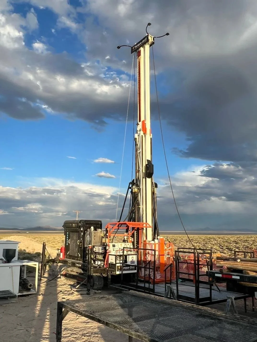 A large drilling rig stands in a desert landscape under a partly cloudy sky.