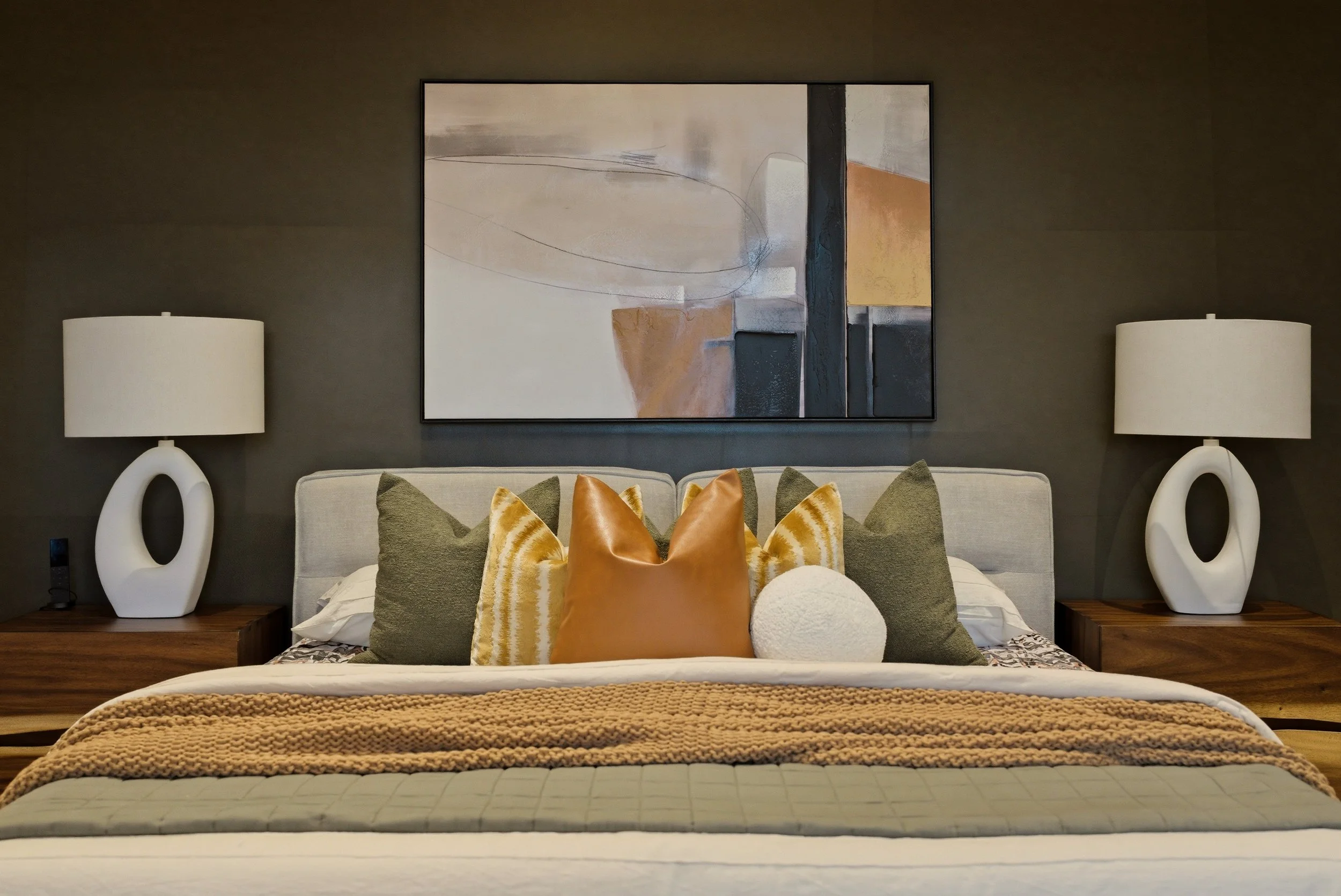 Staged bedroom with a dark accent wall, green and mustard bedding, and warm natural textures.