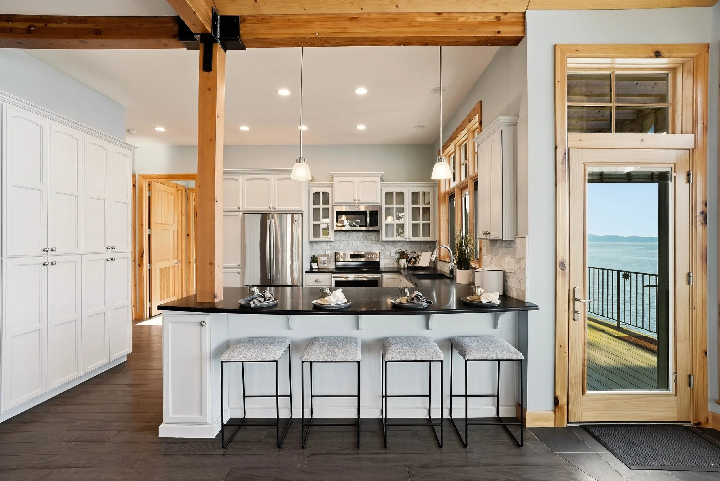 A kitchen beneath a vaulted wood ceiling with white cabinetry and dark counters. Styling by Home Staging Works.