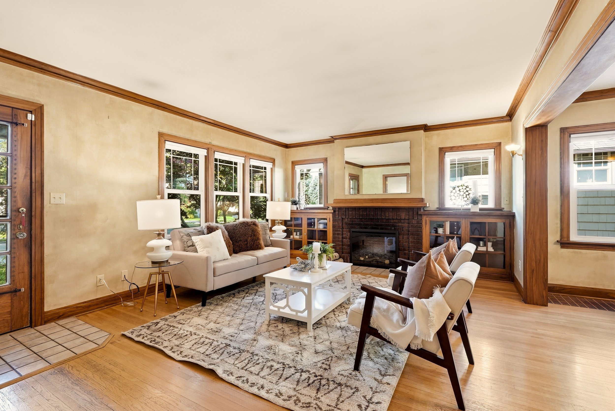 HSW Essentials staging in a Spokane living room with a light sofa, two accent chairs, a patterned rug and original wood trim around a brick fireplace.