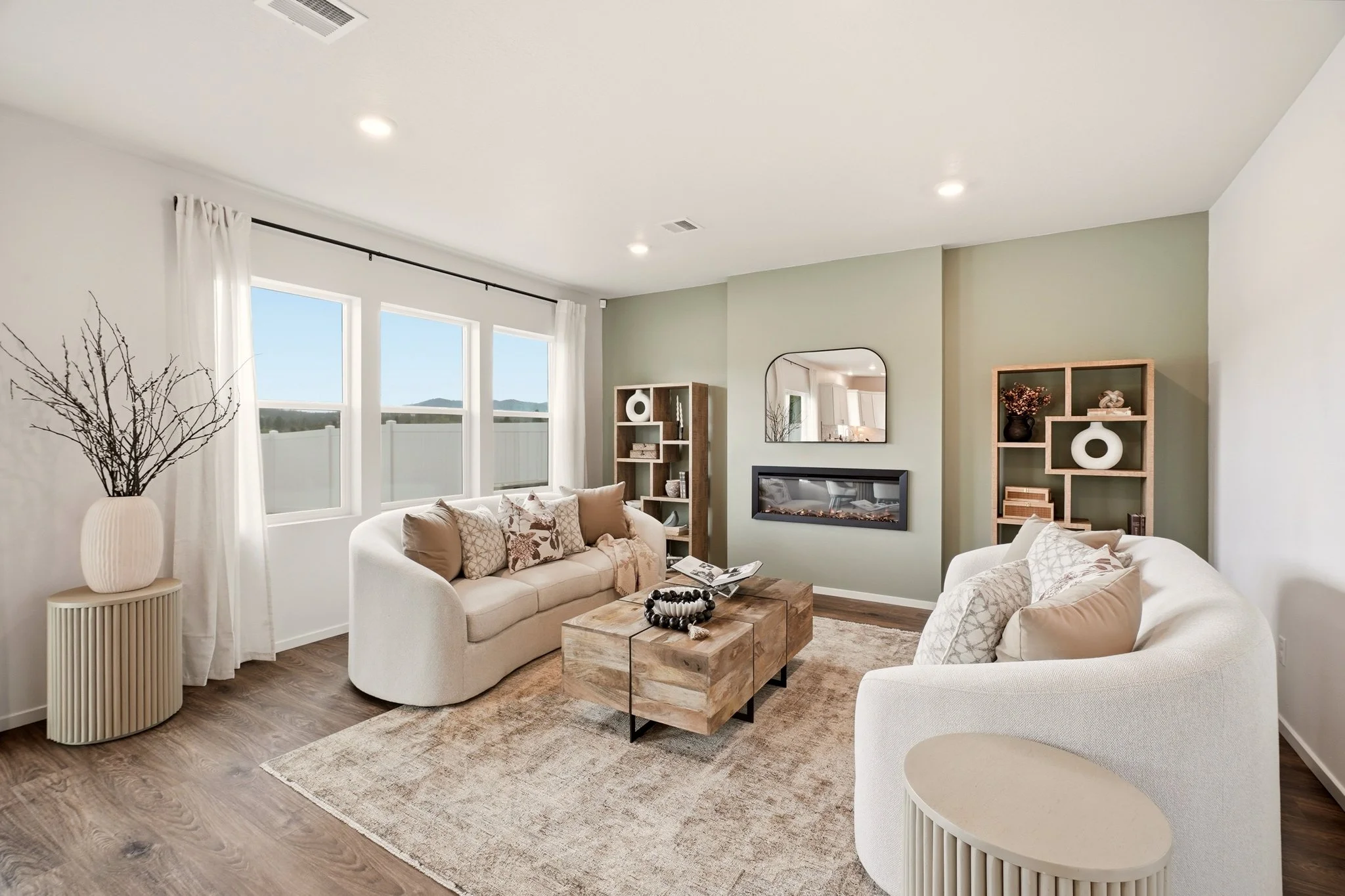 HSW-staged living room with curved cream sofas, a substantial wood coffee table, layered neutral textiles and coordinated shelving around the fireplace.