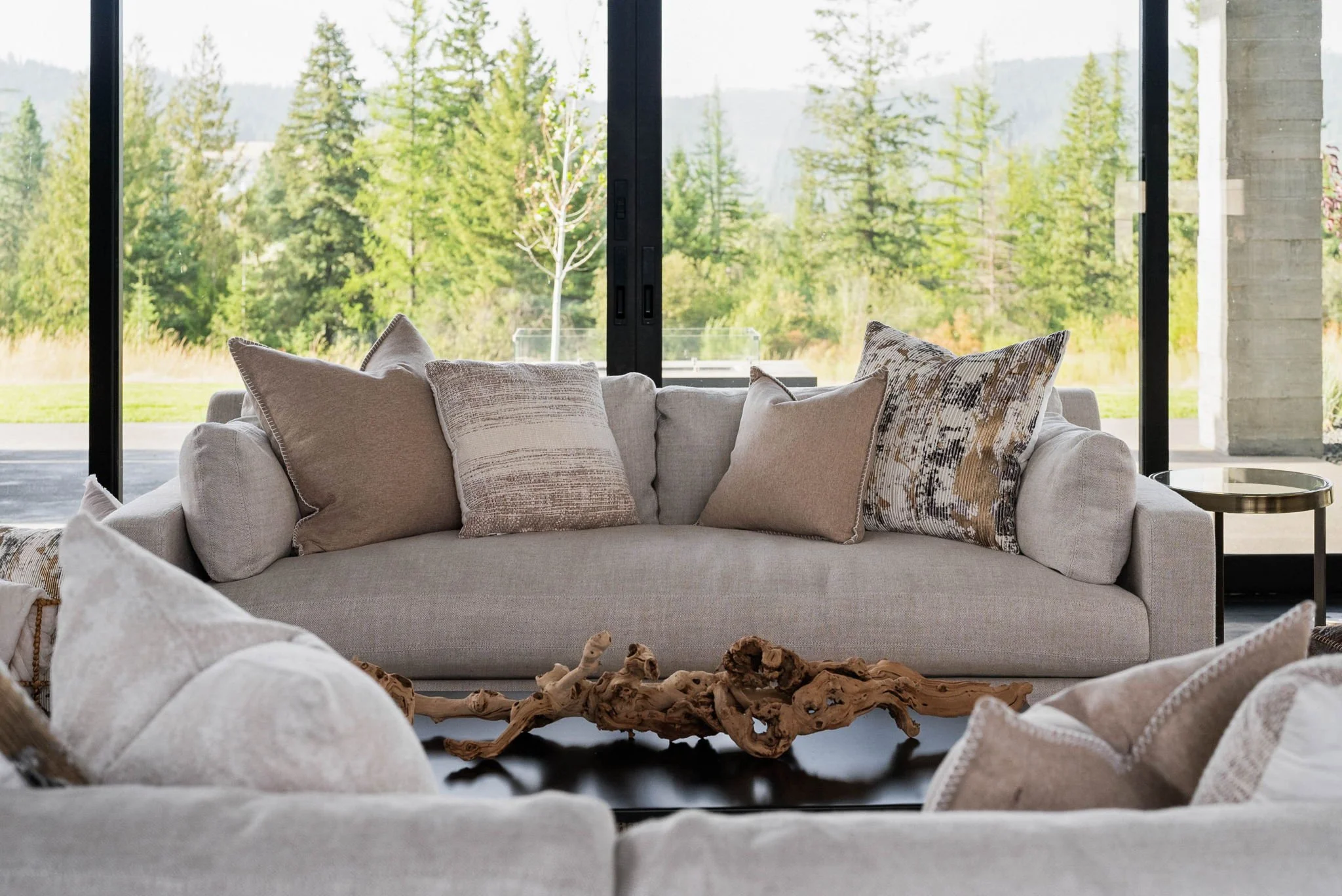 Close‑up of a plush neutral sofa with decorative pillows and a rustic driftwood coffee table in a staged living room, highlighting texture and comfort.
