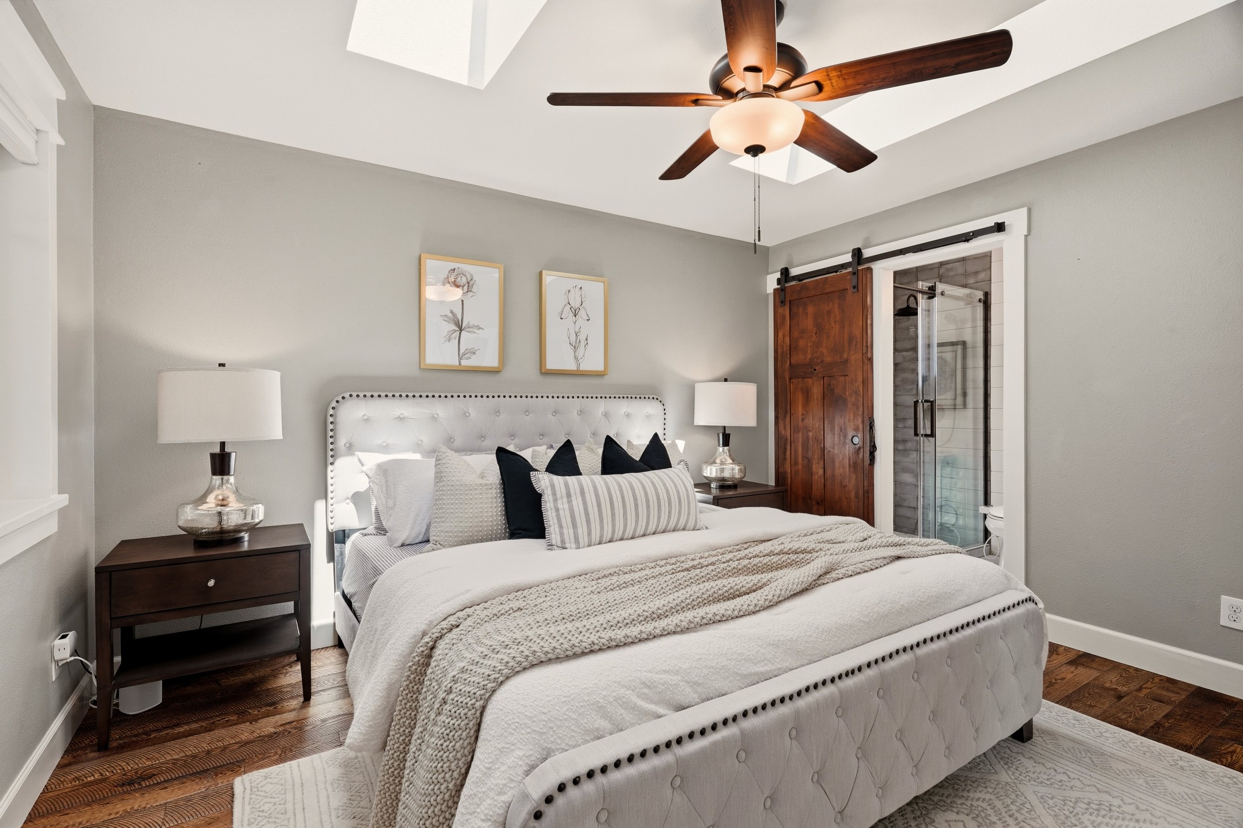 HSW-staged bedroom with layered white bedding, dark nightstands, coordinated lamps and artwork.