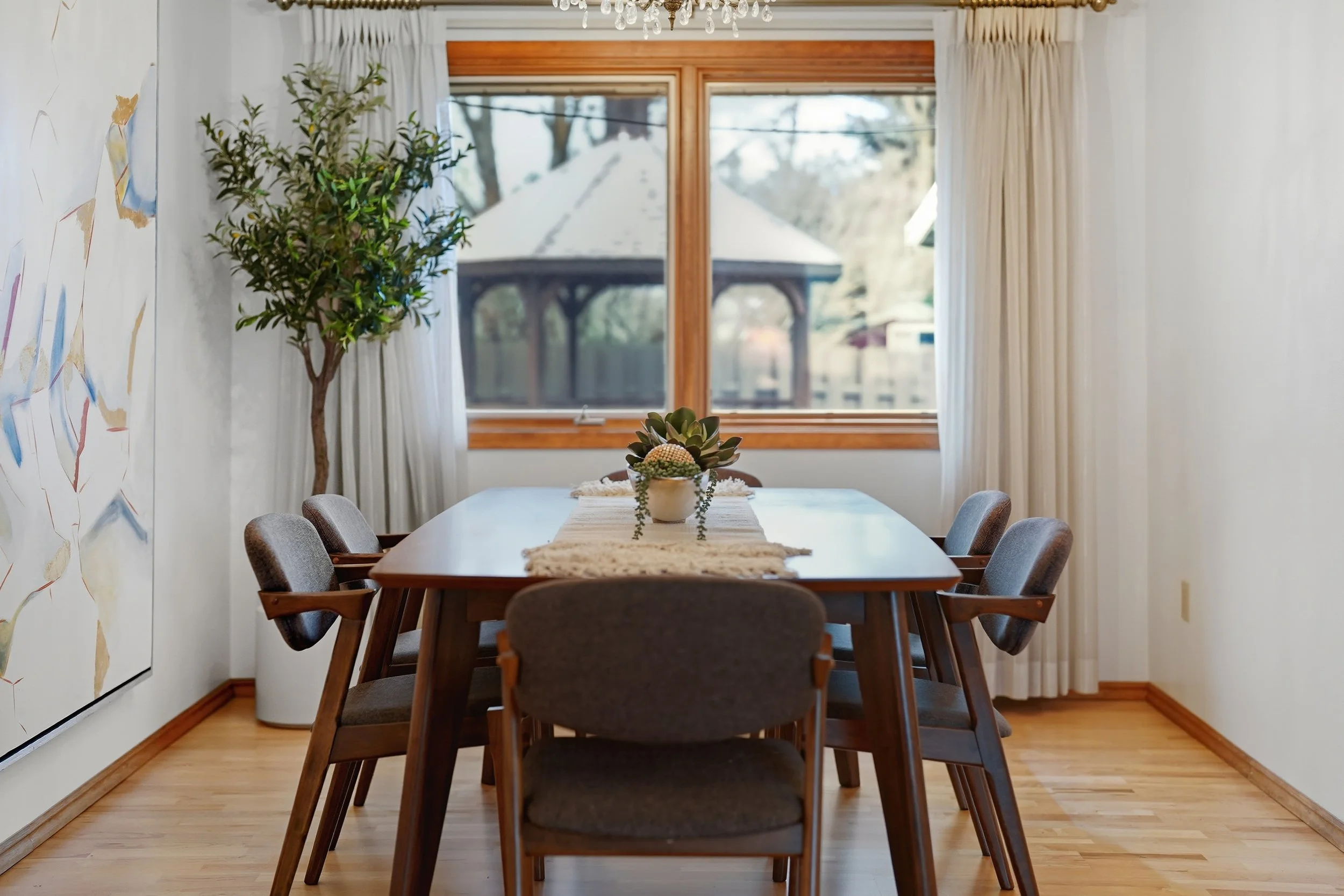 Staged dining room with a wood table, leather chairs, light curtains and warm wood window trim.