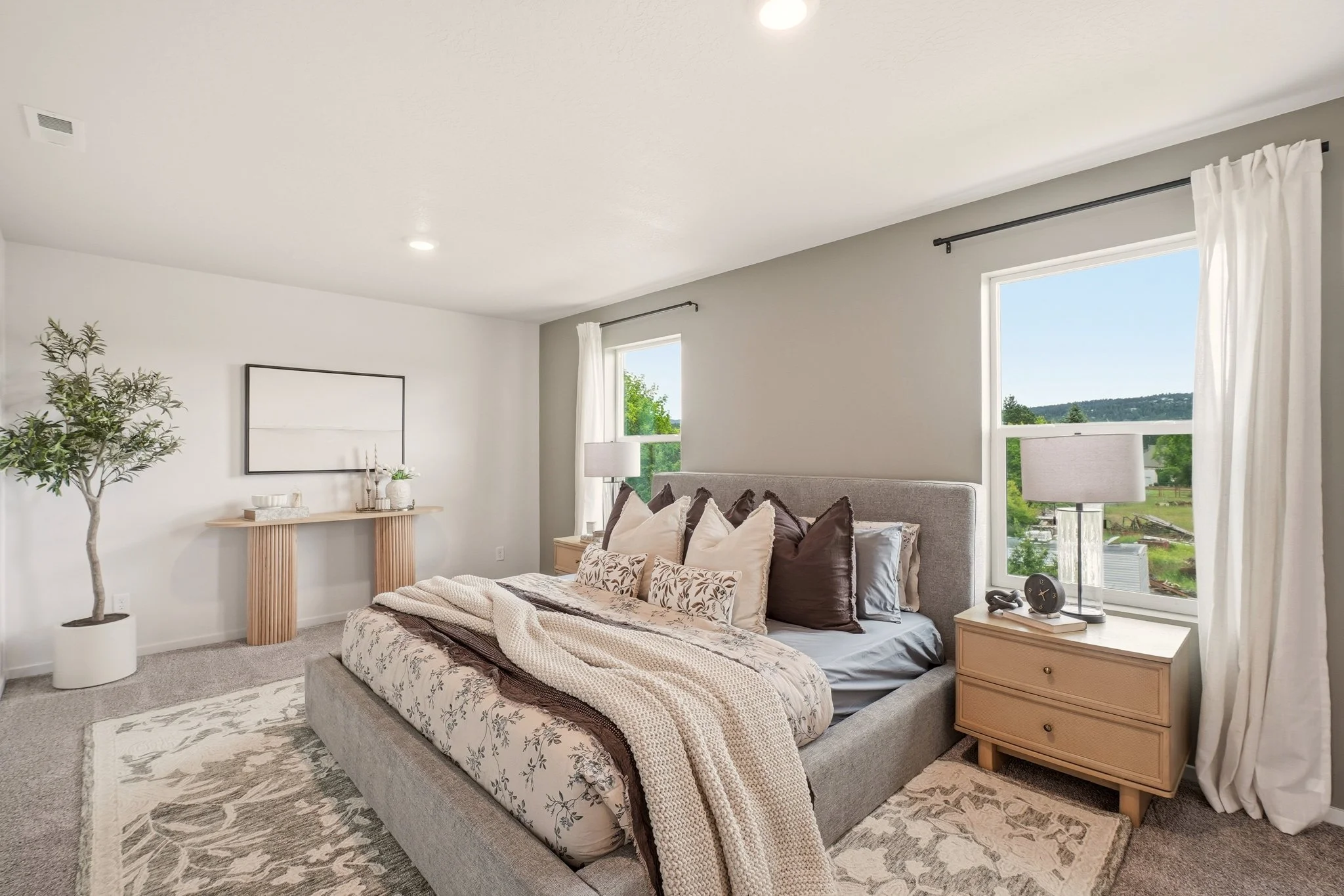 HSW-staged primary bedroom with layered neutral bedding, wood nightstands, matching lamps and a patterned rug.