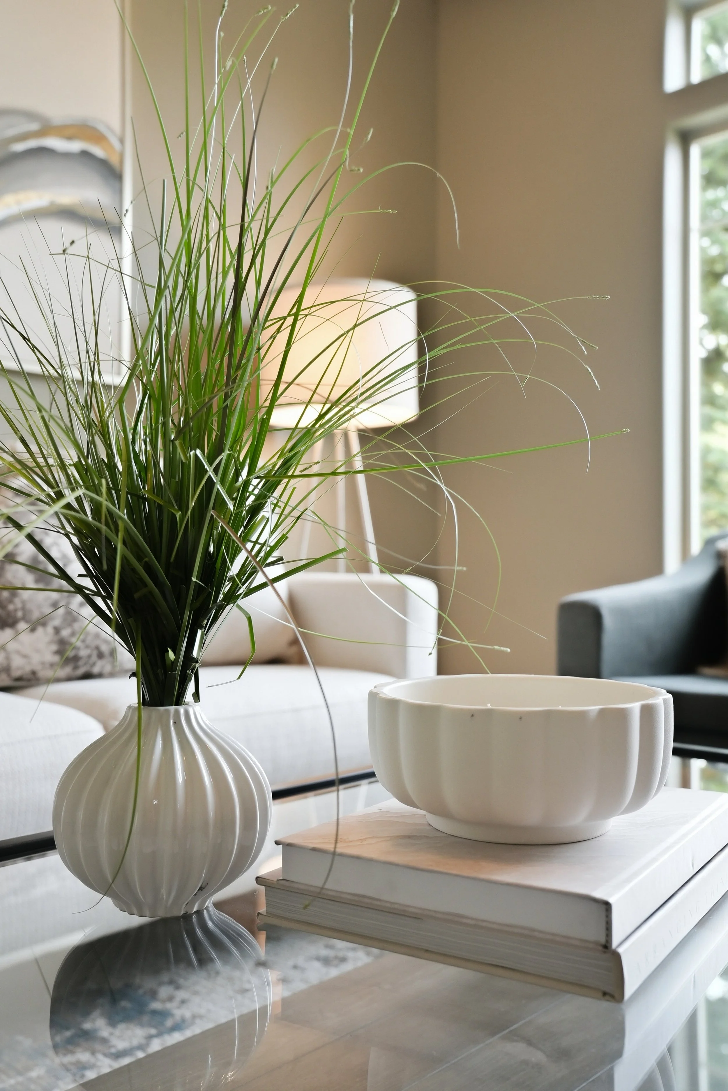 Greenery, books and a white cup on a wood table beside a softly upholstered sofa. Styling by Home Staging Works.