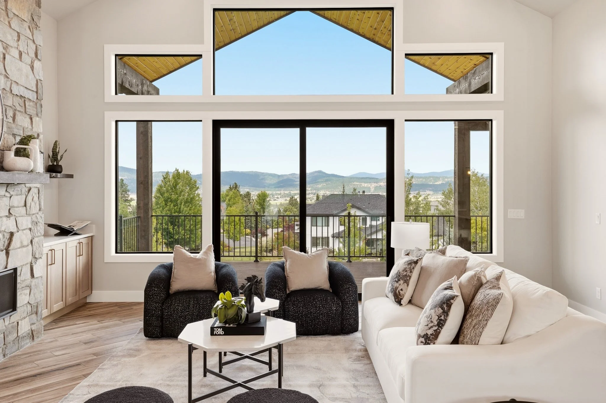 Closer view of HSW’s Signature staging in Liberty Lake, with a cream sofa, layered cushions, textured dark armchairs and nesting tables framed by tall windows.