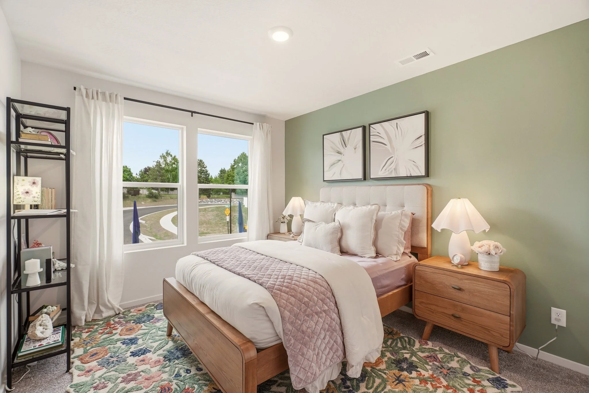 A sage-green bedroom with blush bedding and a wood bedside table. Staging by Home Staging Works.