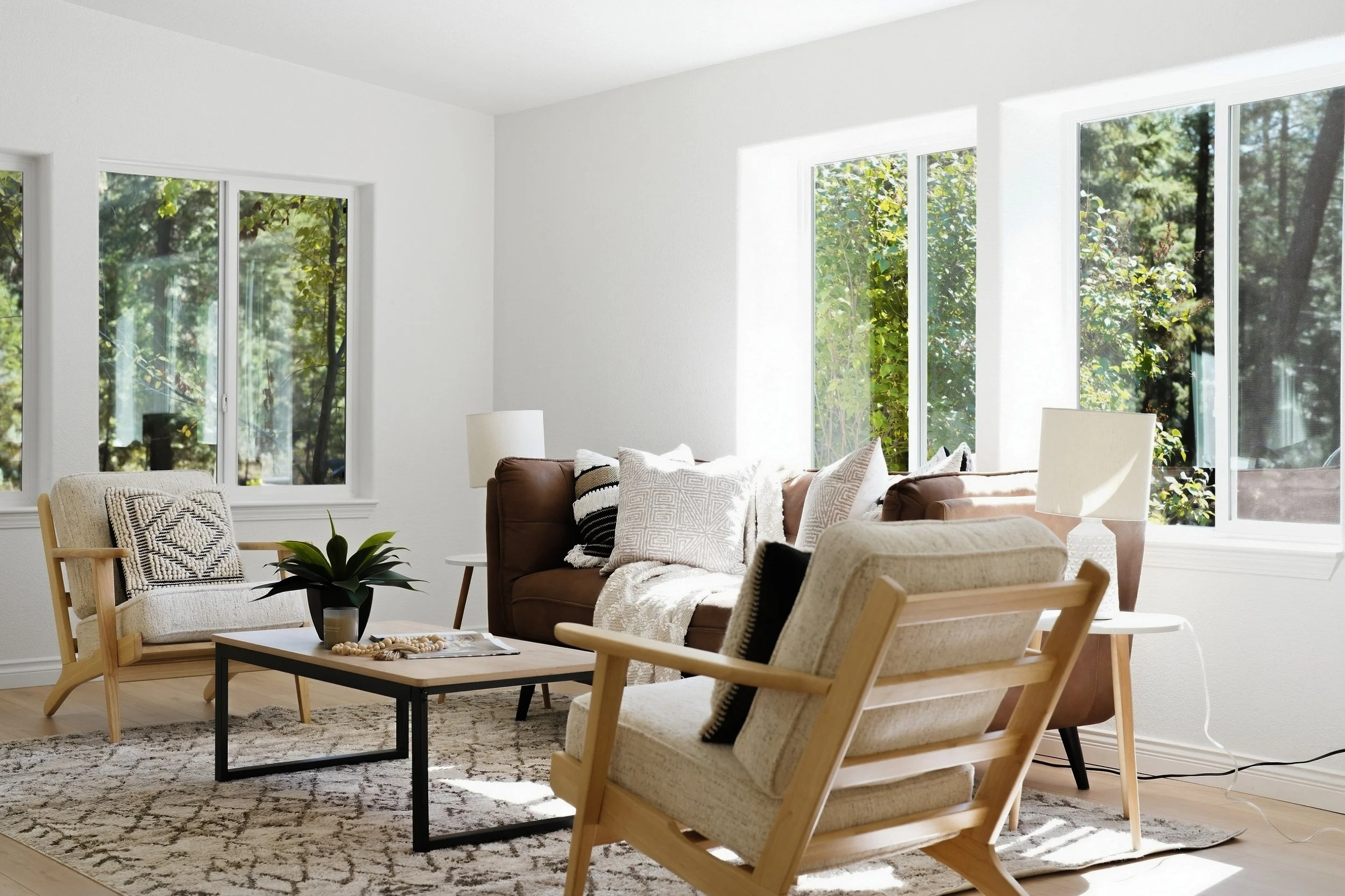 Warm, naturally lit living room staged by Home Staging Works, with a brown sofa, cream chairs, and wood accents. Photography by Inside Media.