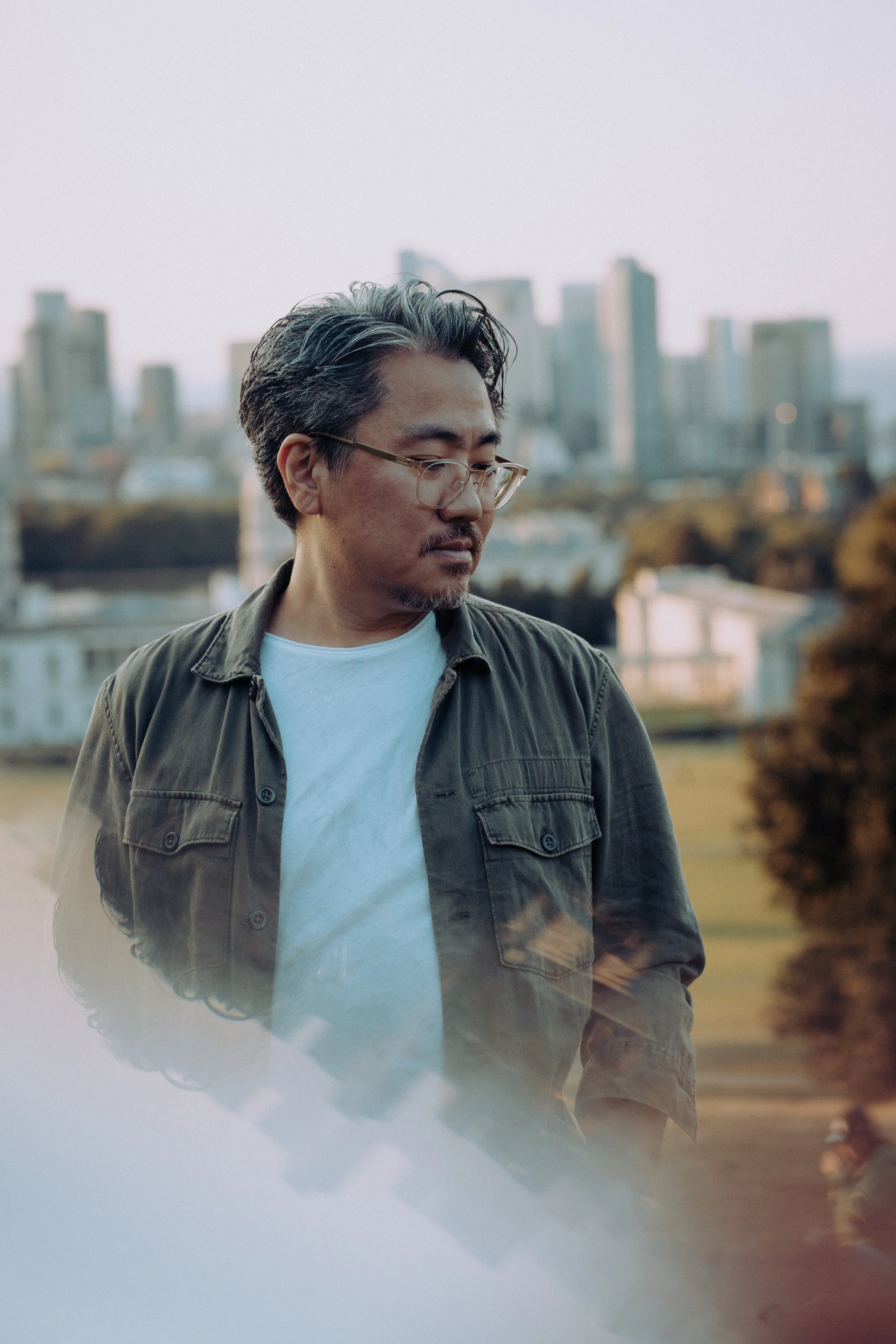 Makoto, drum & bass DJ and producer, wearing glasses and a dark jacket with a city skyline in the background.