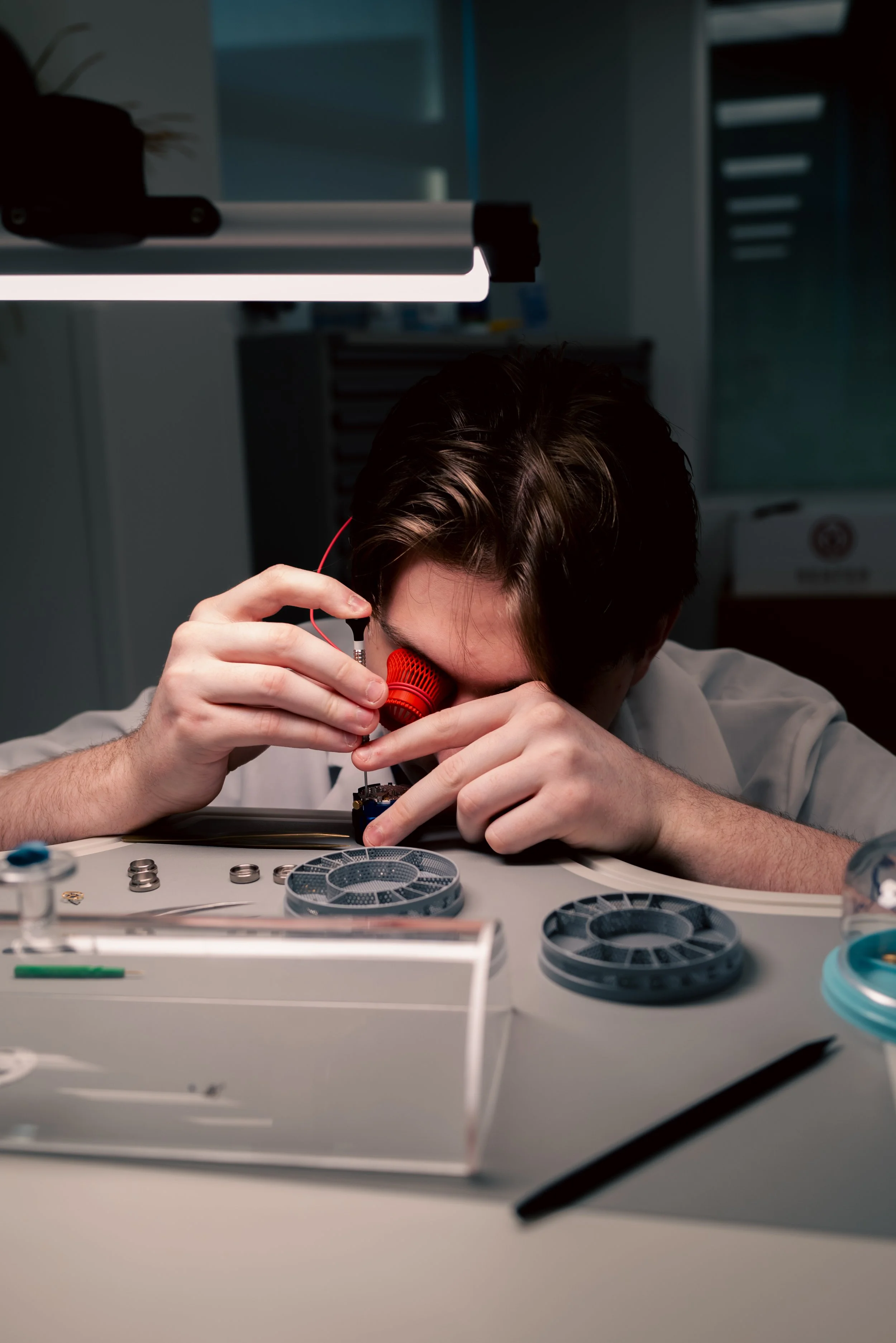 A person working in a laboratory, assembling or repairing a small electronic device with various tools and parts on the table.
