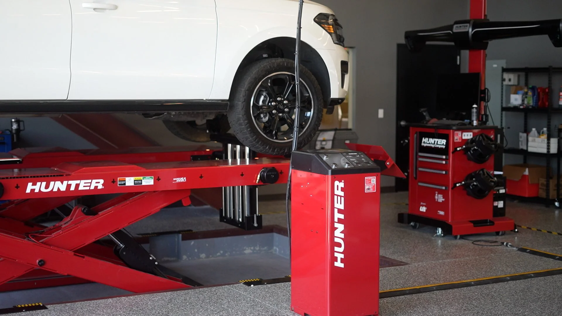 White vehicle elevated on a red Hunter automotive lift in a garage or repair shop.