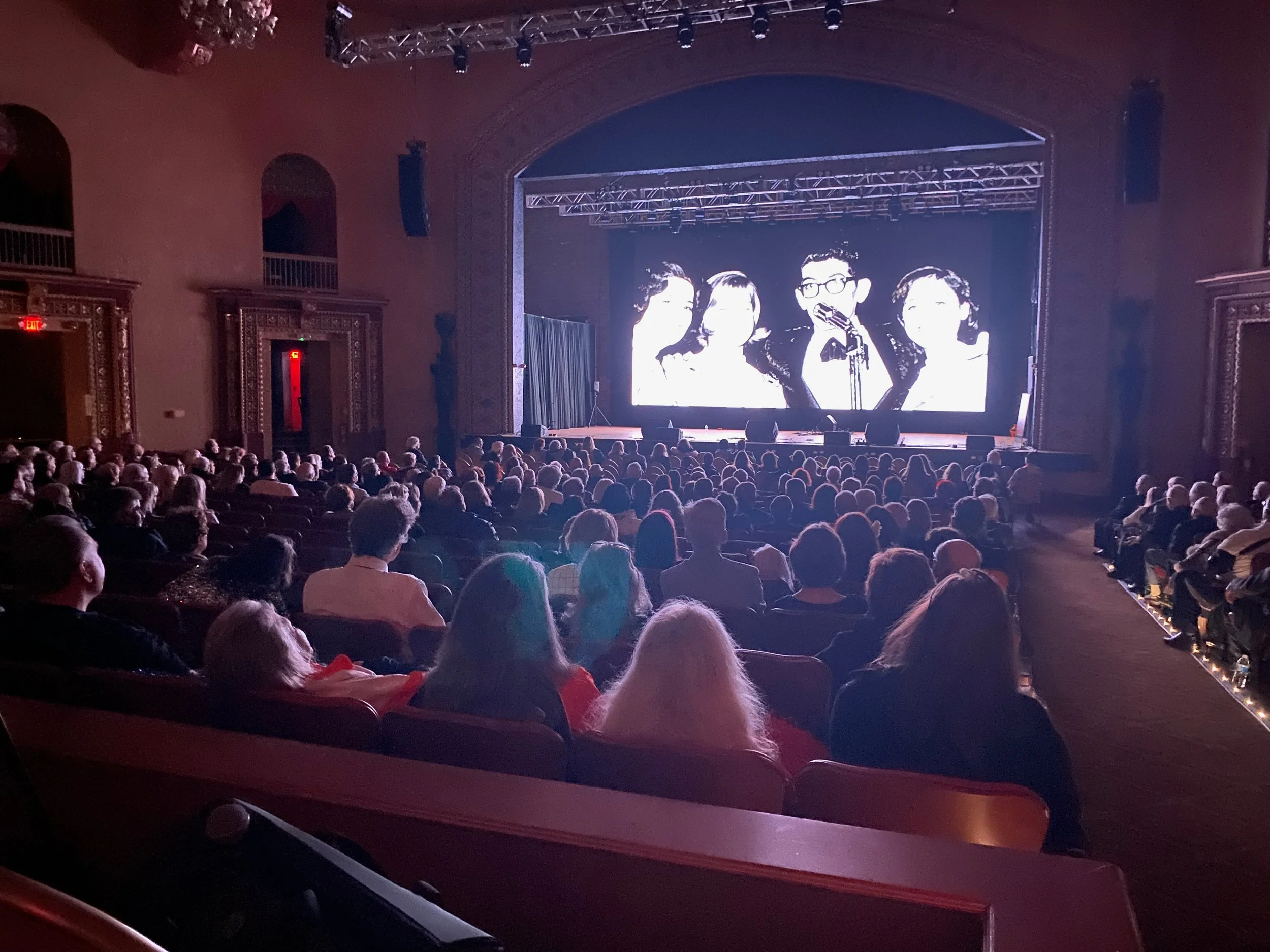 Audience members watching The Voice That Rocked America – The Dick Biondi Story on the big screen at a community screening.