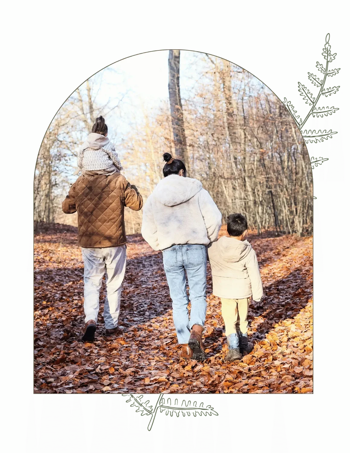 Family walking on a leaf-covered trail in a forest during autumn, with trees in fall foliage.