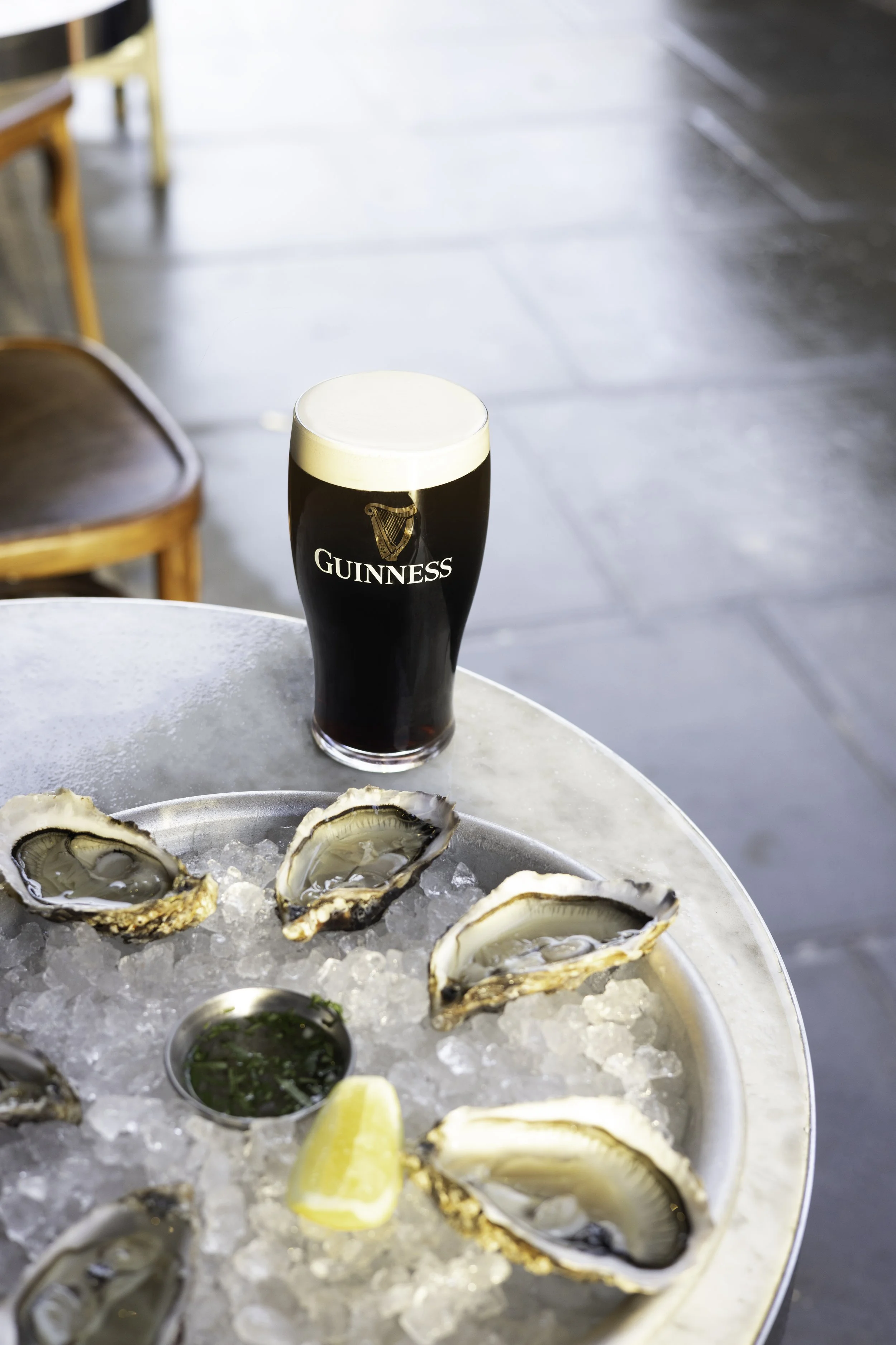 A pint of Guinness beer on a table in a restaurant or bar setting, with a plate of oysters on ice also visible.