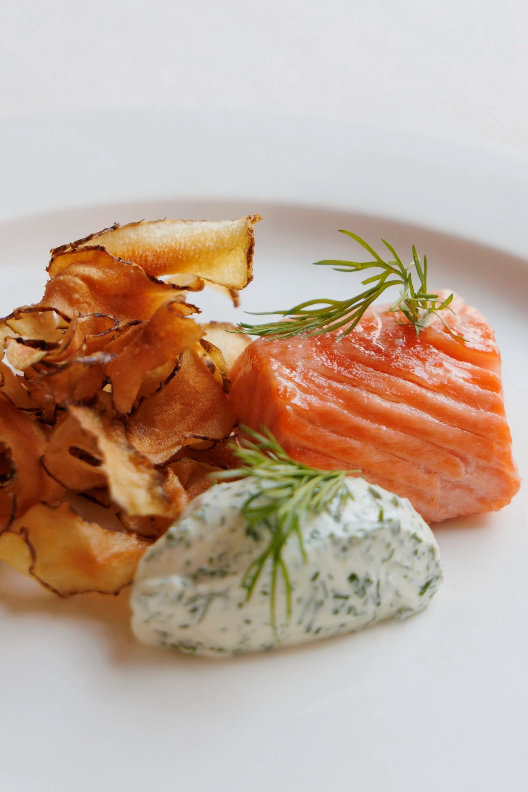 A plated dish featuring seared salmon topped with dill, side of crispy bacon, a dollop of herb-infused cream, and a sprig of fresh dill garnishing the creamy sauce.