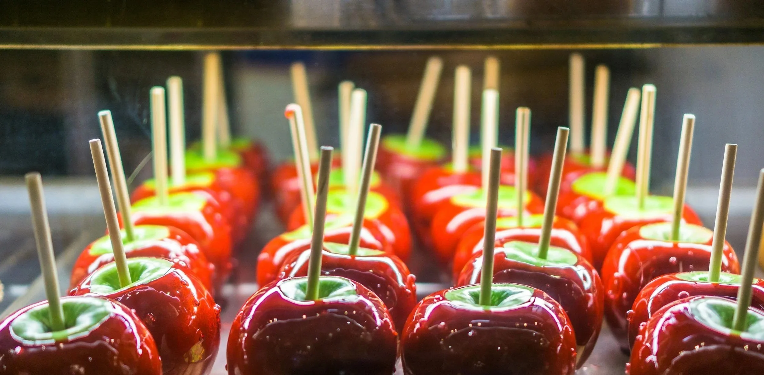 A tray of red candy apples with green apples and a bright red caramel-candy coating, each with a wooden stick for holding.