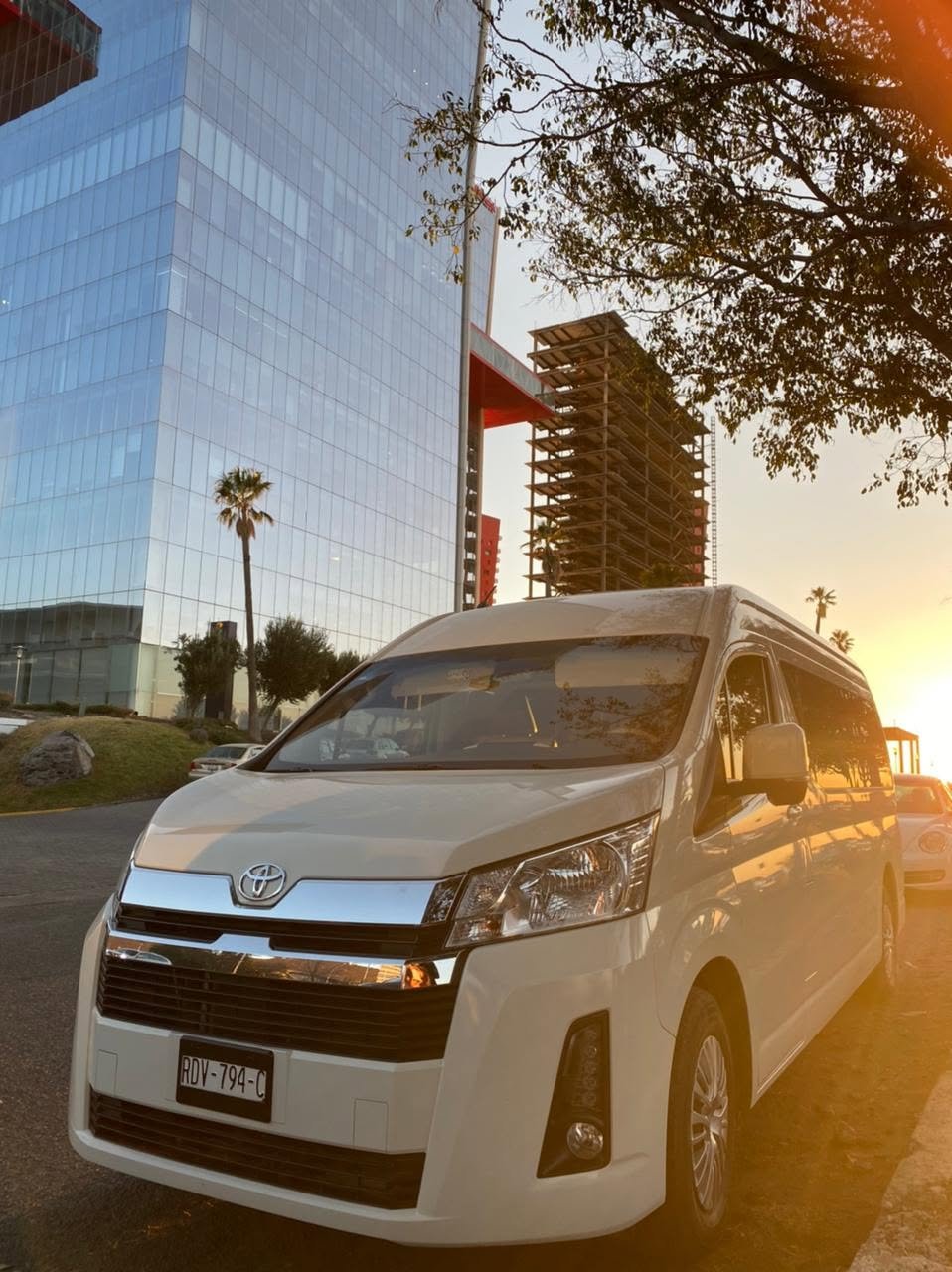 Una camioneta blanca Toyota estacionada en una avenida al atardecer con edificios de vidrio y palmeras en el fondo.