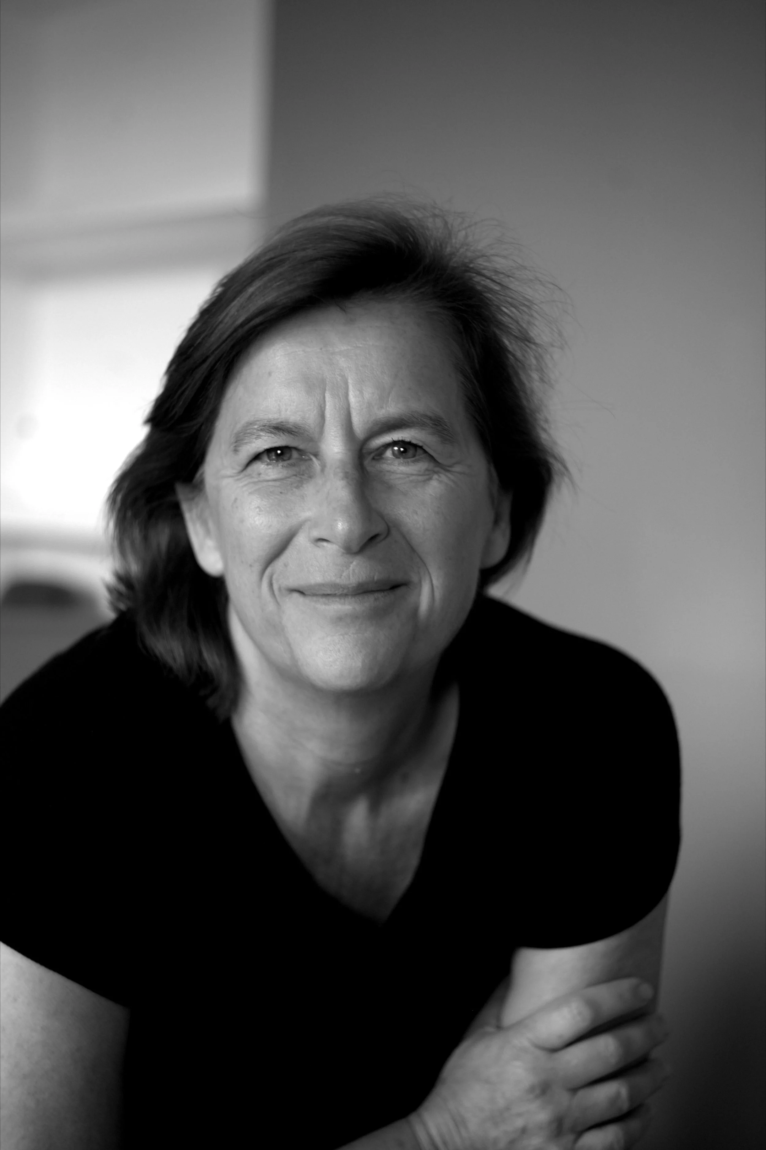 Une femme souriante en noir et blanc, montrant partiellement son visage et ses épaules et portant un haut noir.