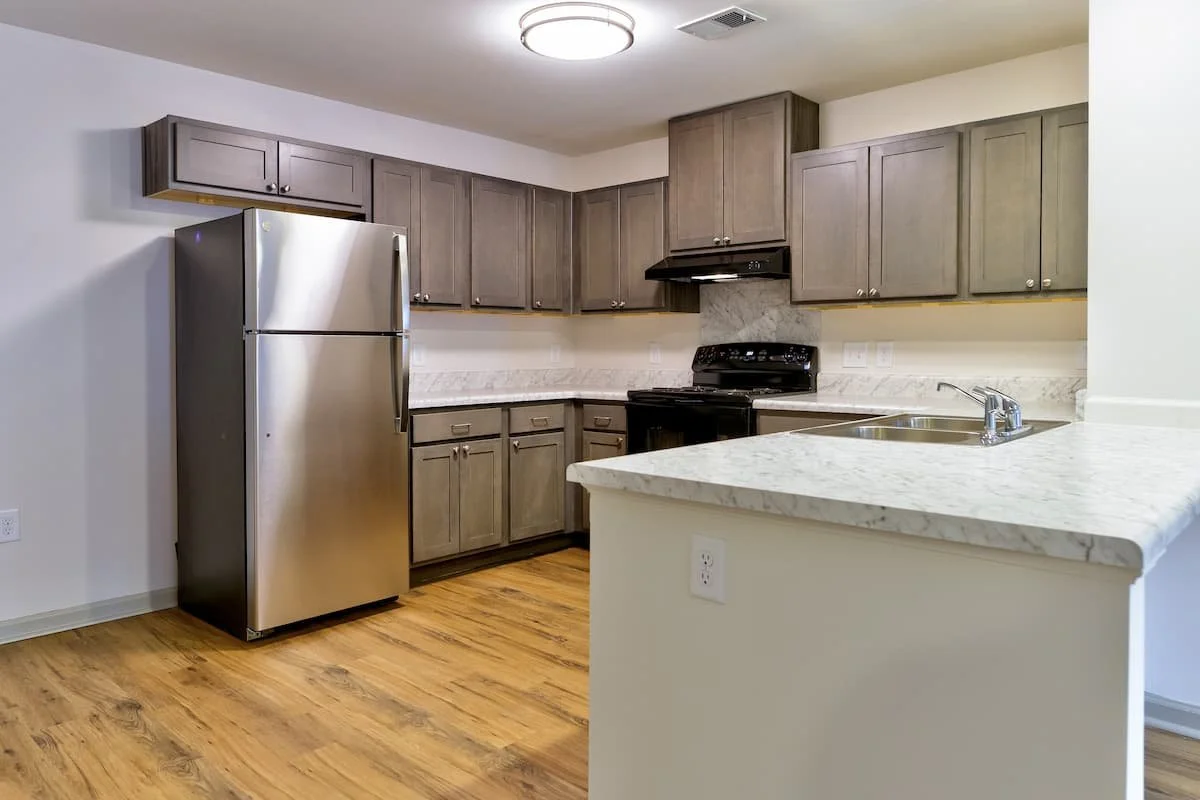 Modern kitchen with gray cabinets, stainless steel refrigerator, black stove and range hood, marble countertops, and wood flooring at Birch & Branch Apartments in Raleigh, NC.