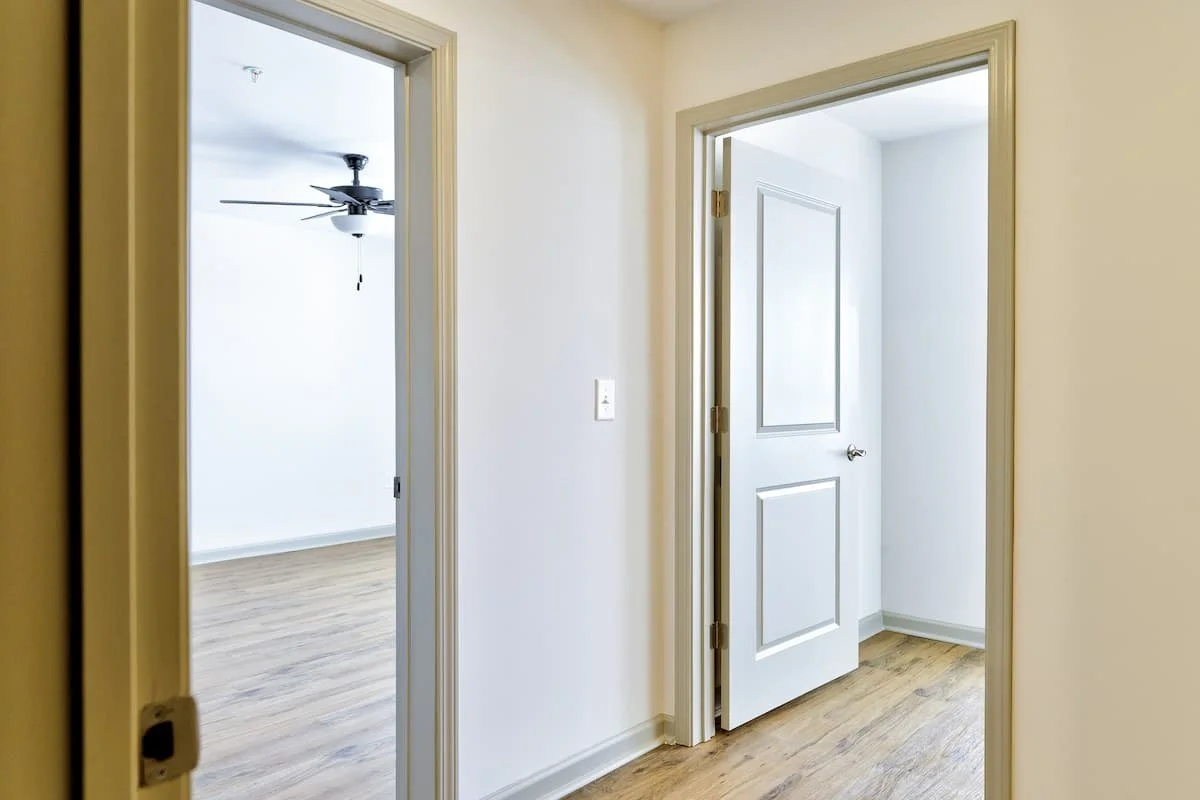 View of two doorways from a hallway into bedrooms, one room has a ceiling fan, hardwood floors, and white walls at Birch & Branch Apartments in Raleigh, NC.
