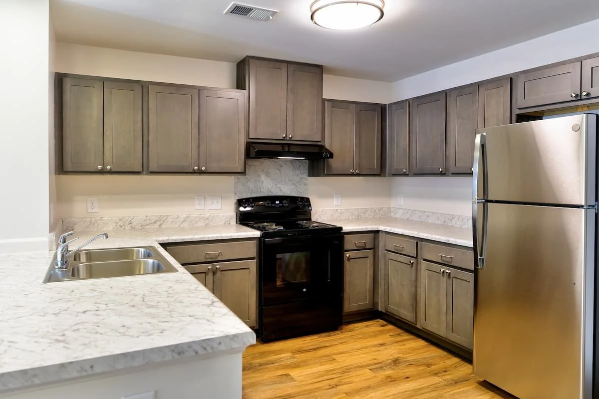 Kitchen at Birch & Branch Apartments with gray cabinetry, marble countertops, stainless steel refrigerator, black stove, and wooden flooring.