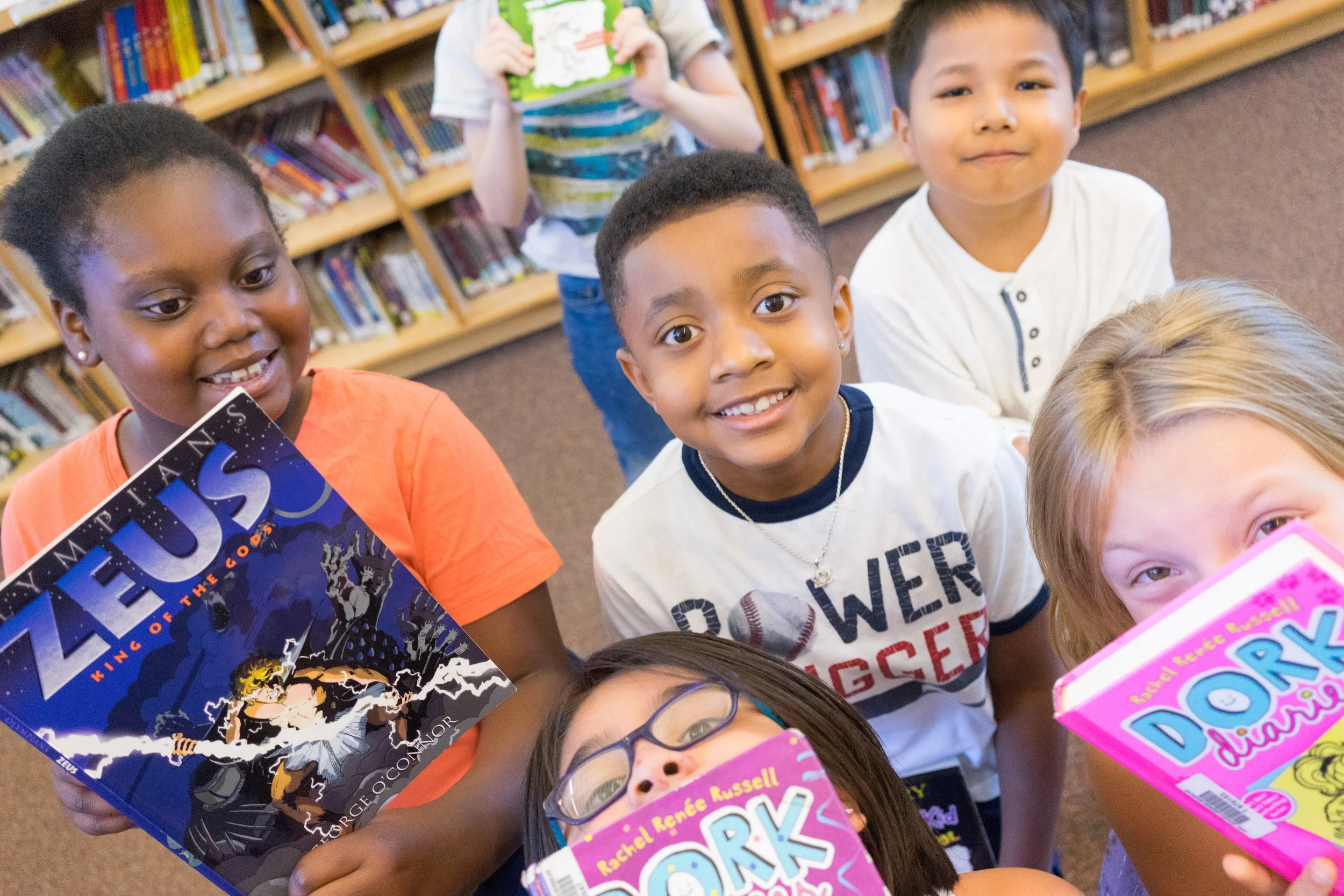 Diverse group of children smiling and holding books in a school library