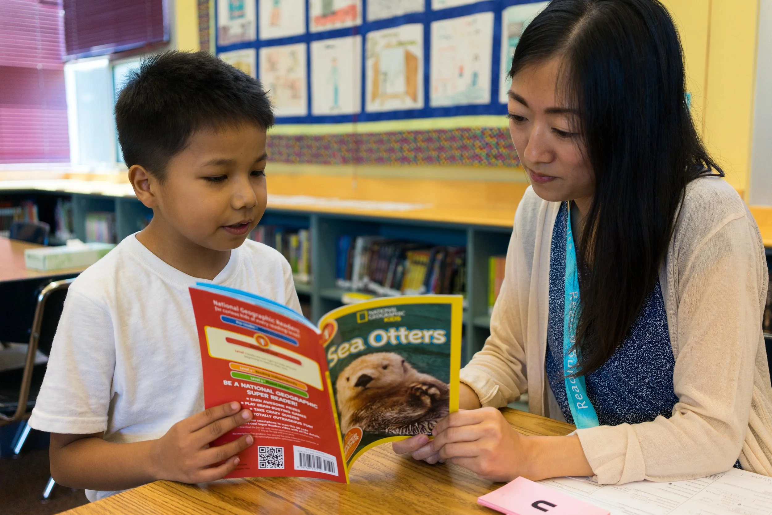 Teacher reading a sea otter book with a young student in a classroom