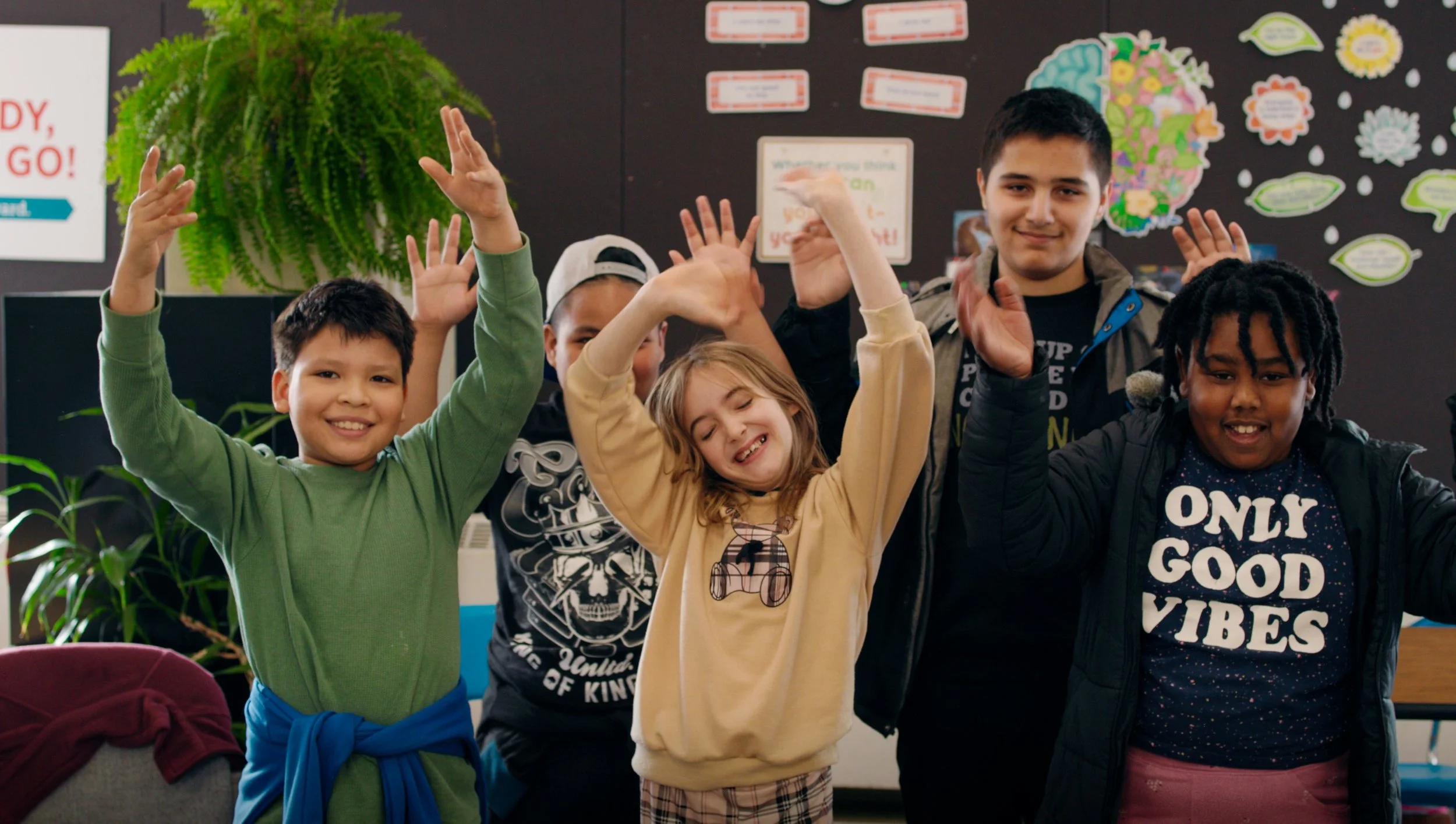 Diverse group of children smiling and raising their hands in a decorated classroom