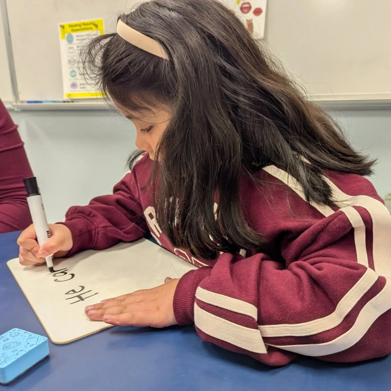 Student writing numbers on a whiteboard at a classroom table