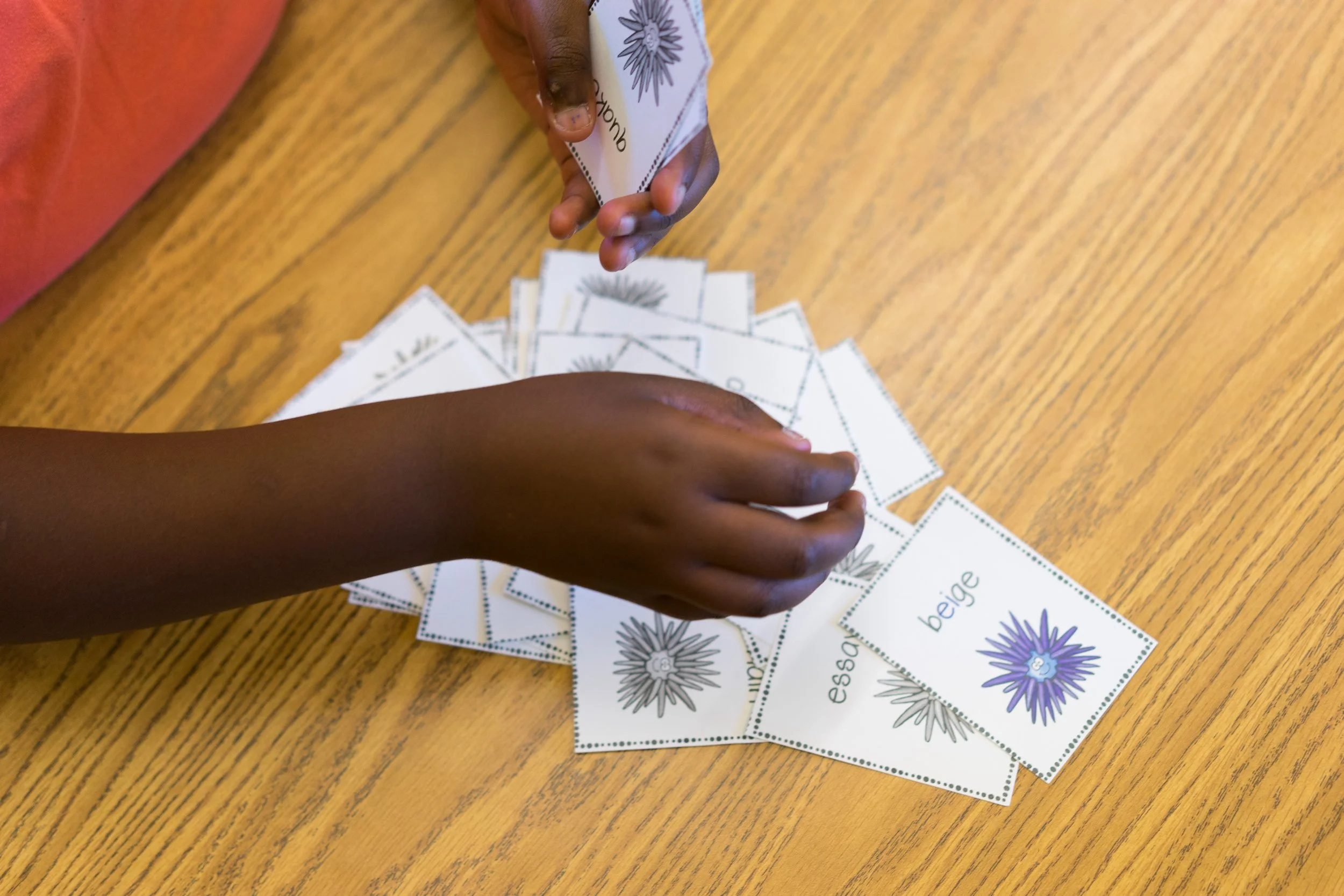 Children sort illustrated word cards on a wooden table during a classroom literacy activity.