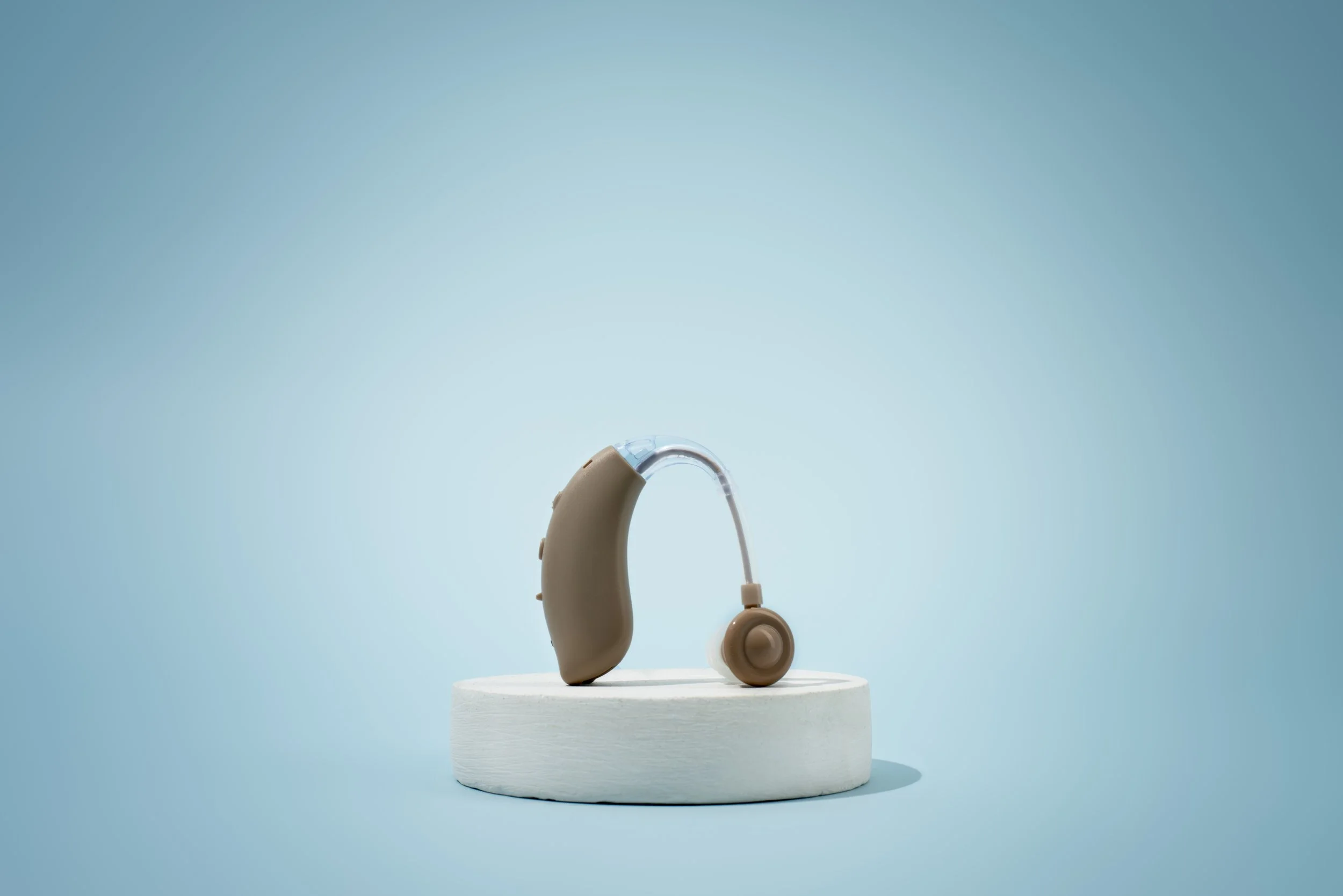 Medical hearing aid placed on a white circular platform against a light blue background.
