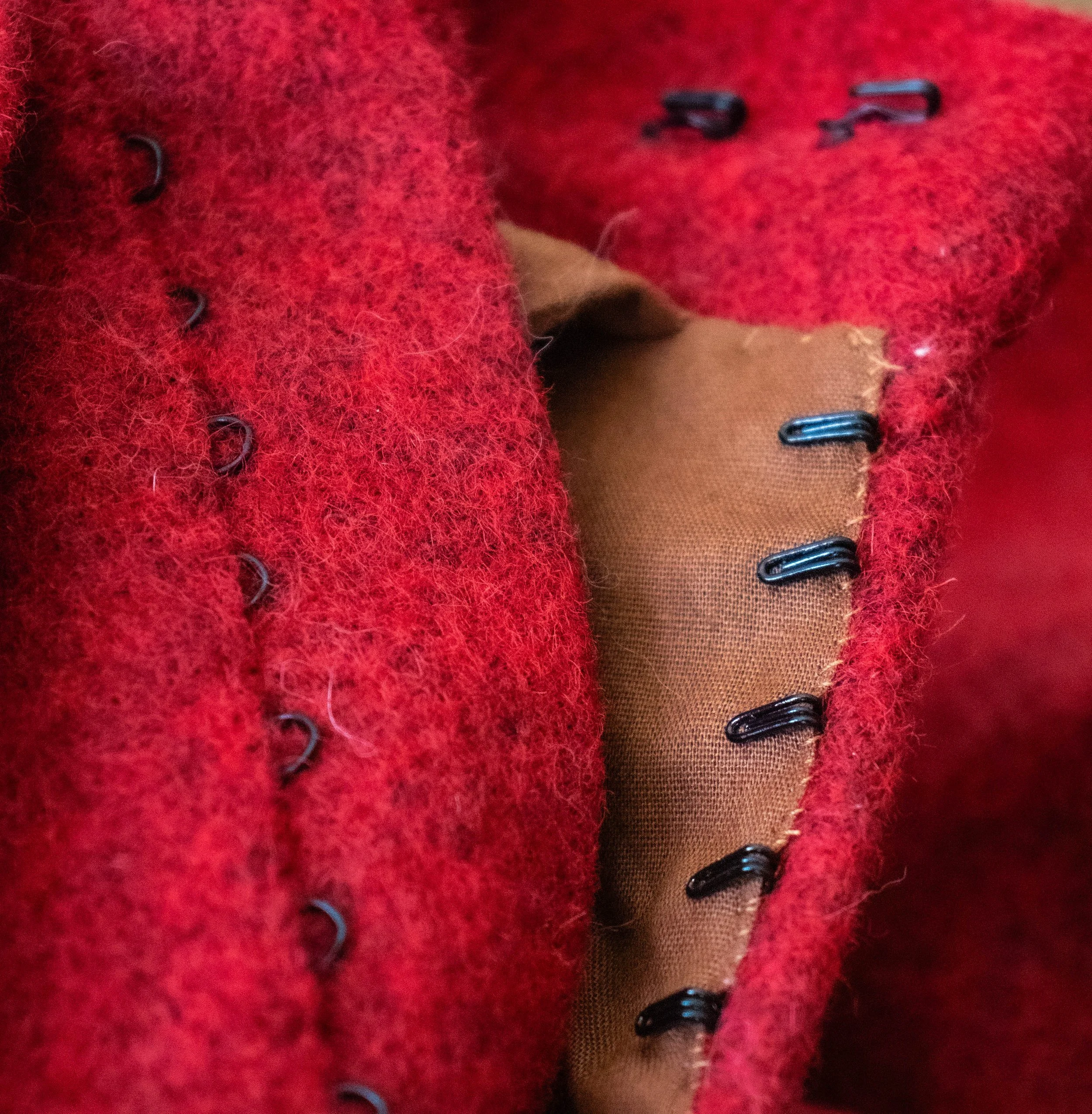 Zoom sur un vêtement en laine rouge avec des boutons en métal, un tissu beige et une partie de nylon
