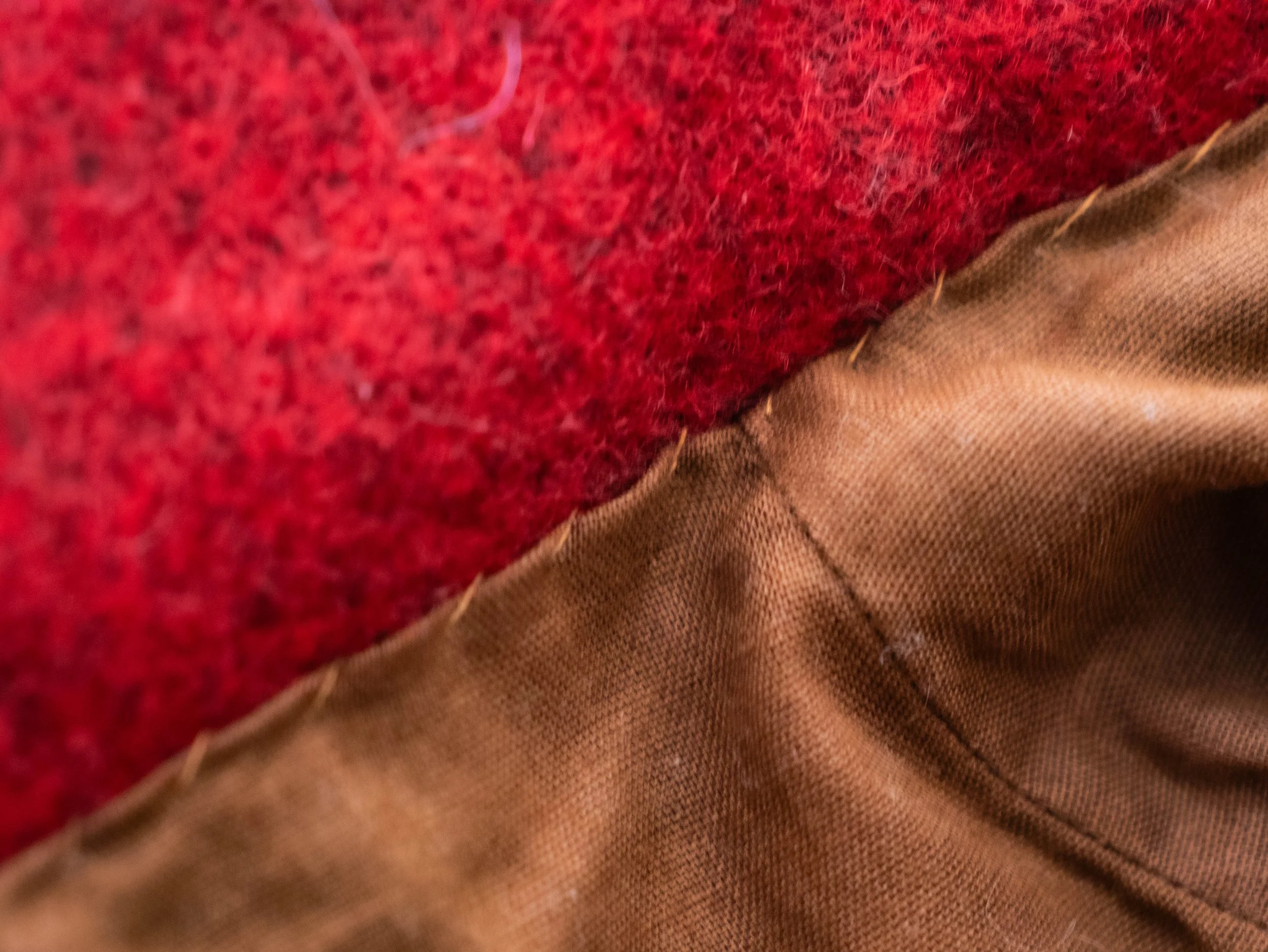 Close-up of red and beige fabric with textured fibers and visible stitching.