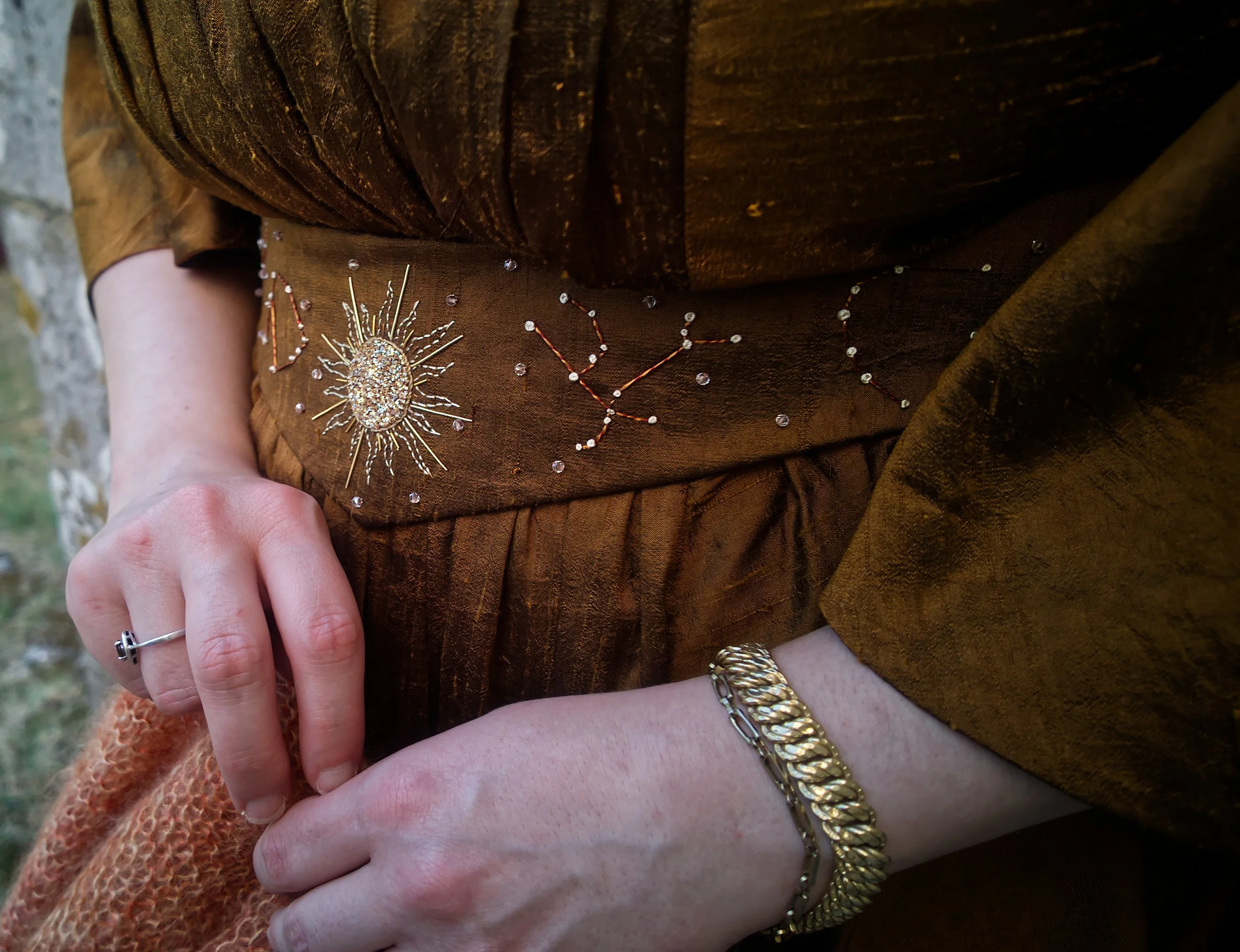 Gros plan d'une personne portant une robe marron ornée de bijoux en forme de soleil et de constellation.
