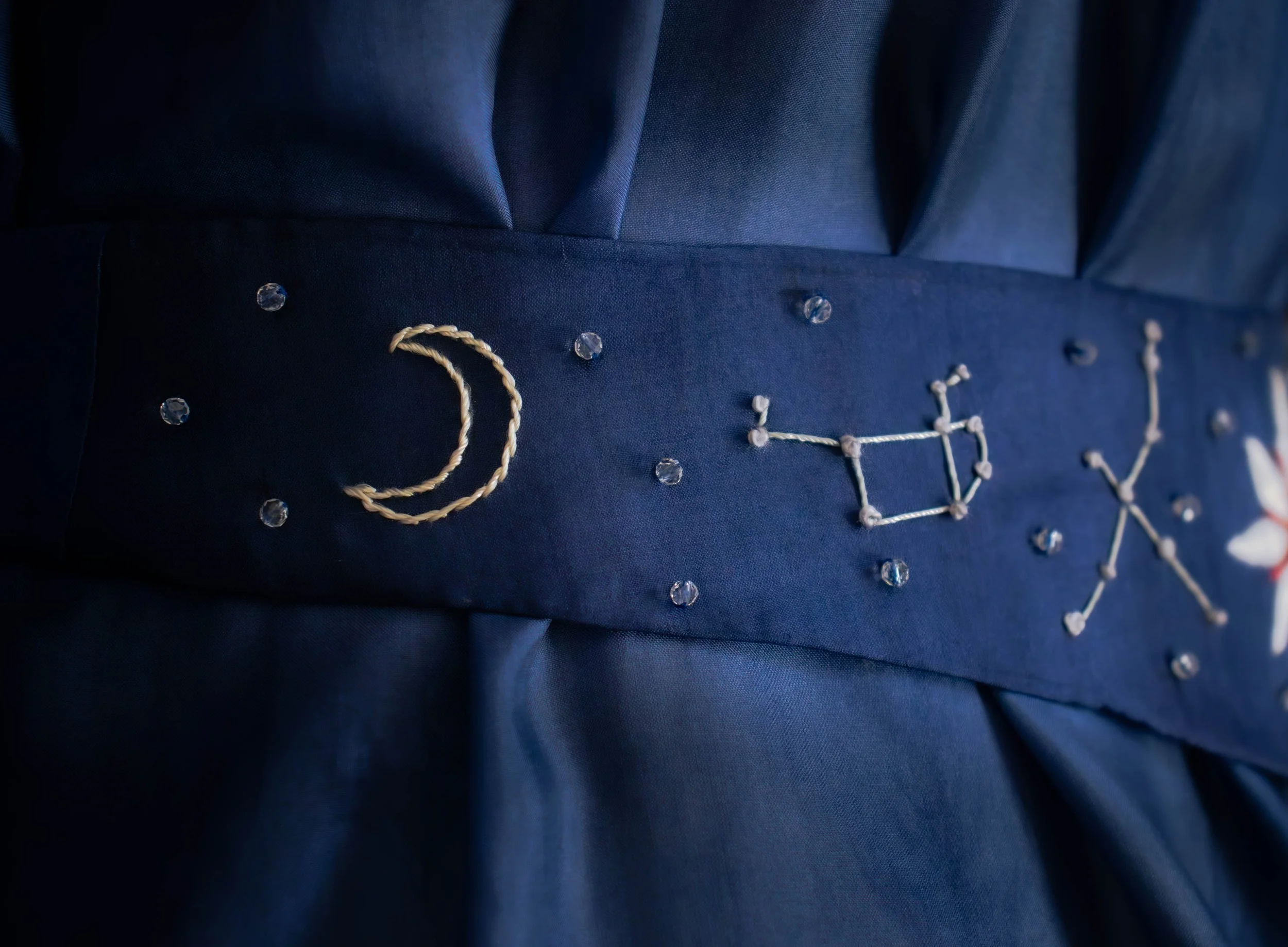Détails proches d'un vêtement bleu foncé avec des décorations en perles et en corde, formant le mot "Doux".