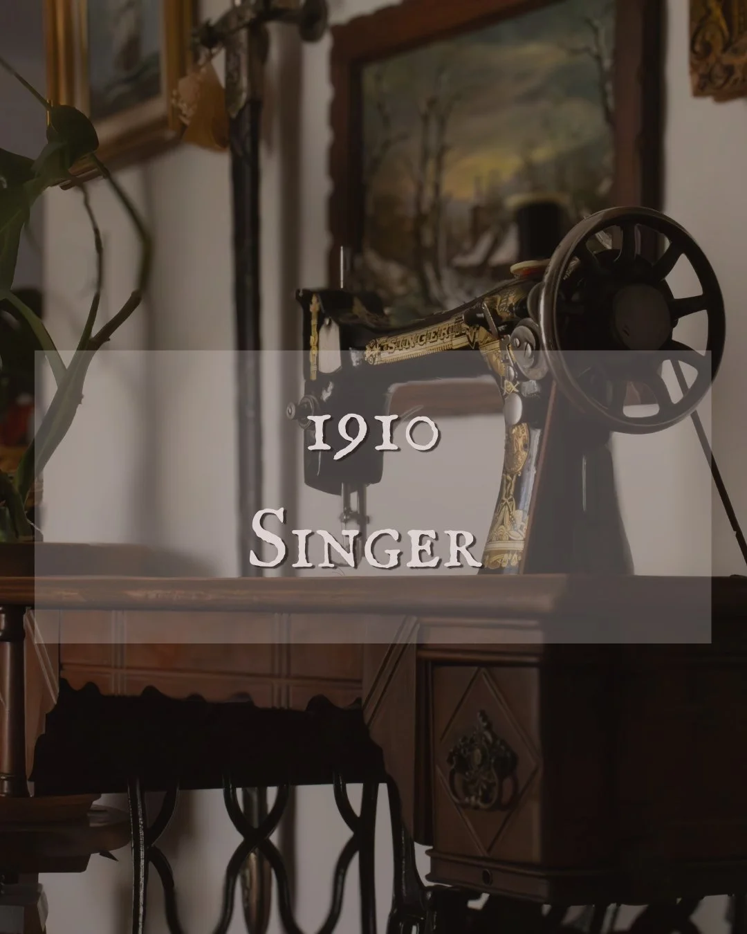 Une vieille machine à coudre sur une table en bois, avec un tableau de paysage en arrière-plan, et une plante sur le côté gauche, avec la mention '1910 SINGER'