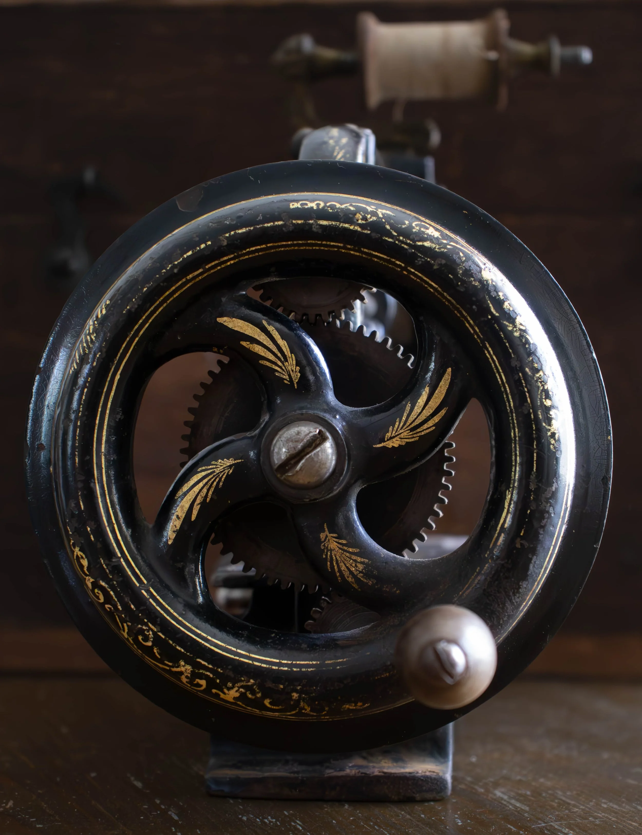 volant de machine à coudre ancienne en ornementations décoratives noirs et dorées, vue plongeante, posée sur une surface en bois