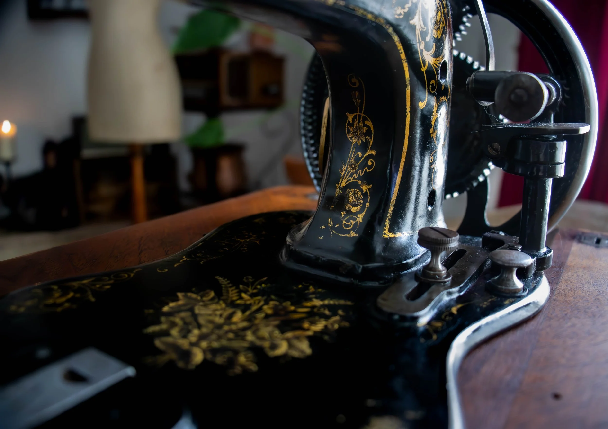 Machine à coudre ancienne noire avec des motifs dorés, posée sur une table en bois.