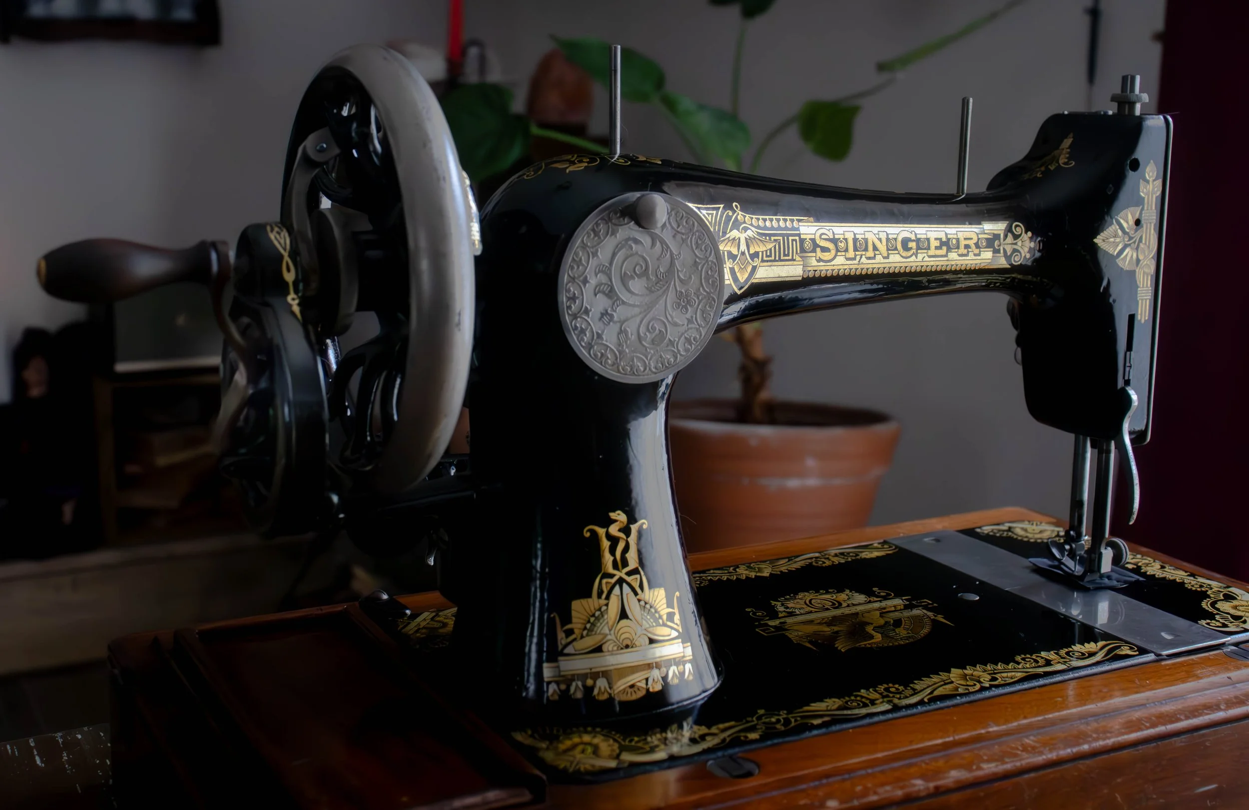 Une machine à coudre ancienne de couleur noire avec des ornements dorés, posée sur une surface en bois.