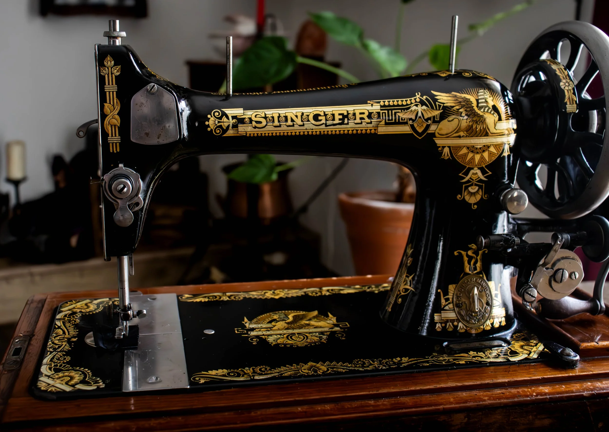 Une machine à coudre ancienne noire ornée de motifs dorés, portant le mot 'SINGER' en lettres dorées, placée sur une table en bois.
