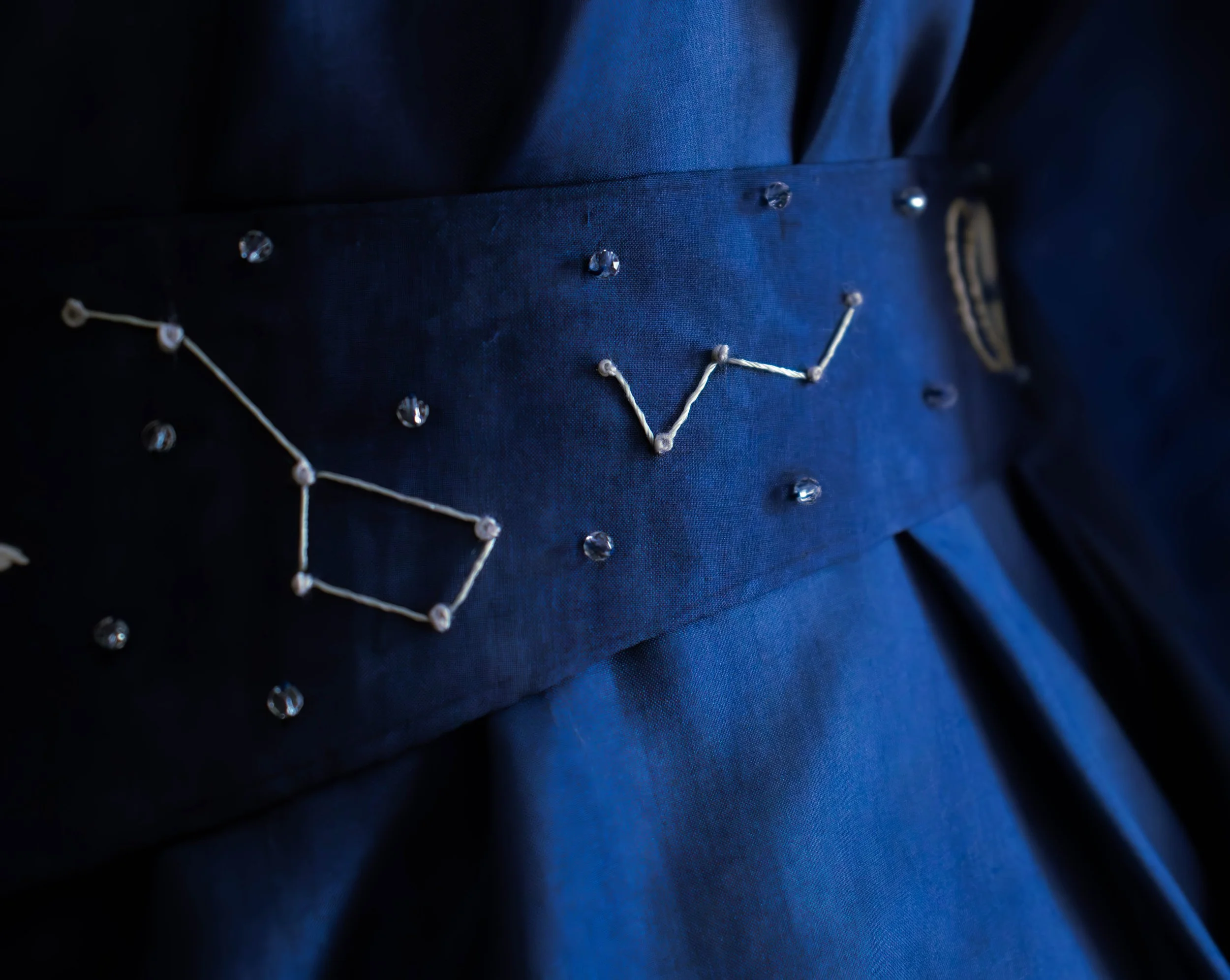 Gros plan d'une veste bleue avec des détails en strass et des broderies blanc cassé.