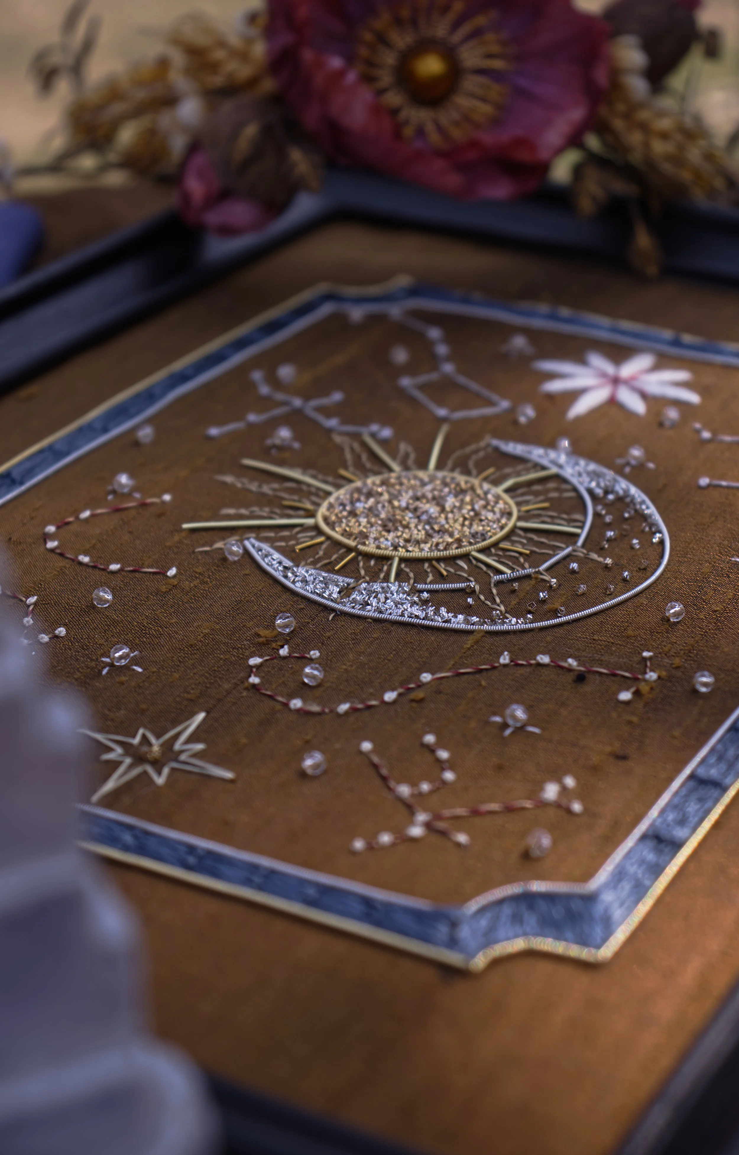 Ornements de décoration, comprenant des étoiles, des fleurs, des perles et des accessoires en métal argenté et doré, disposés sur une surface en tissu marron.