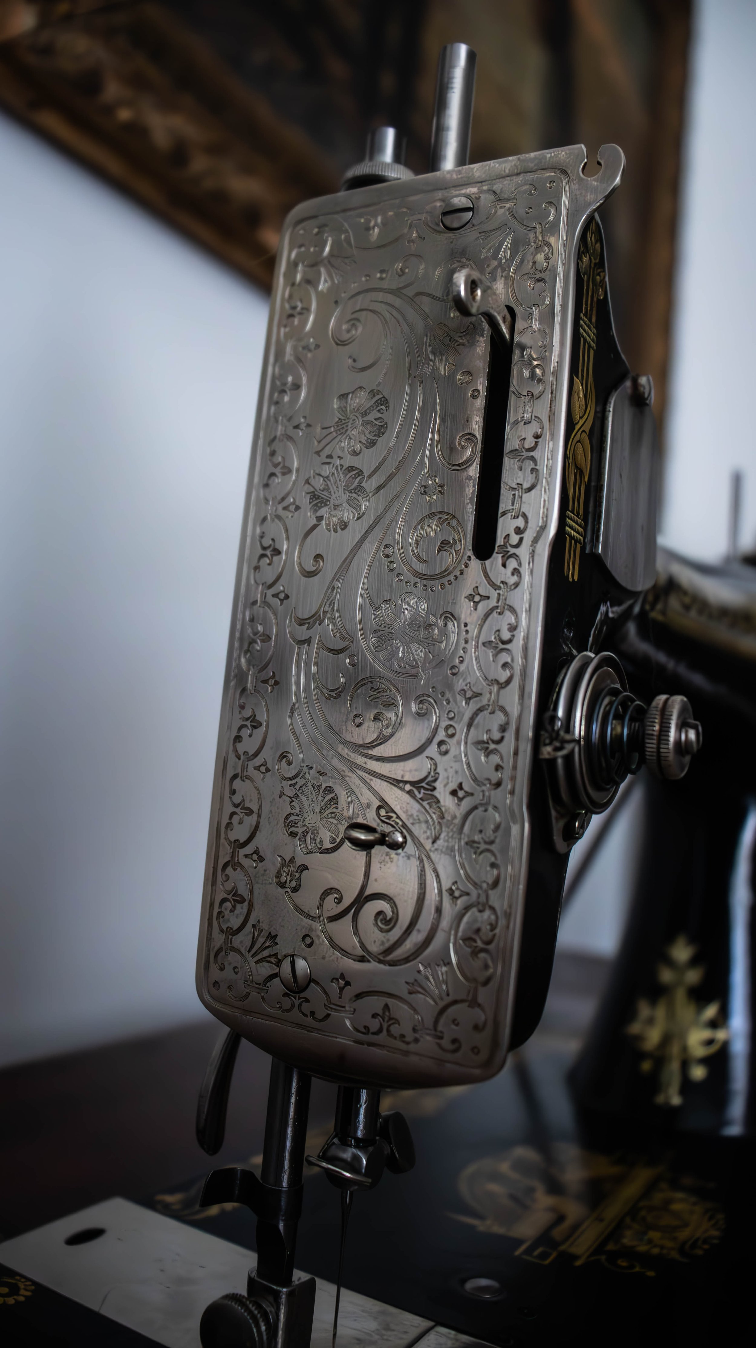 Machine à coudre ancienne avec un boîtier en métal orné de motifs floraux gravés.