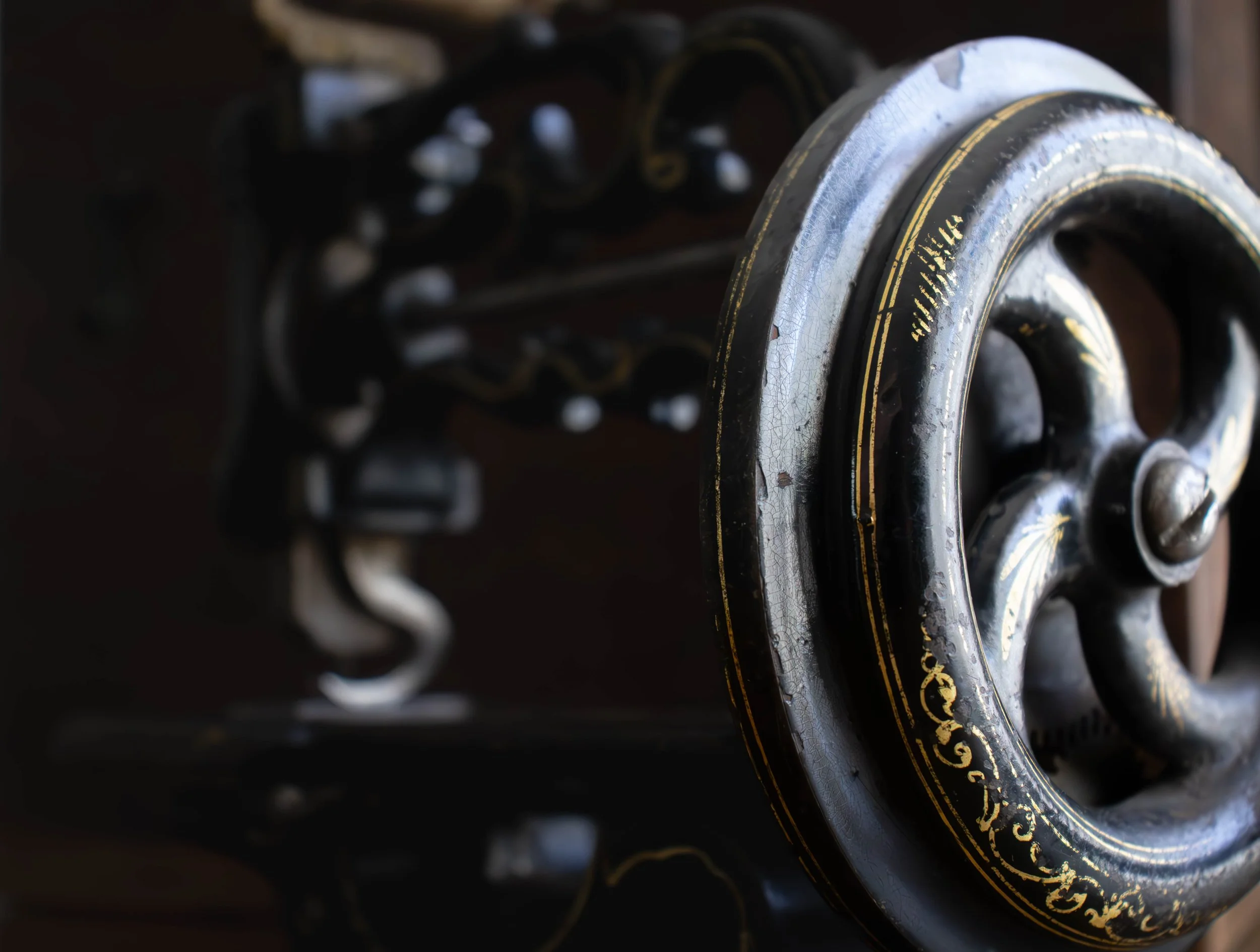 Vu décalée d'une vieille machine à coudre en métal ornés de motifs dorés, créant une composition artistique.