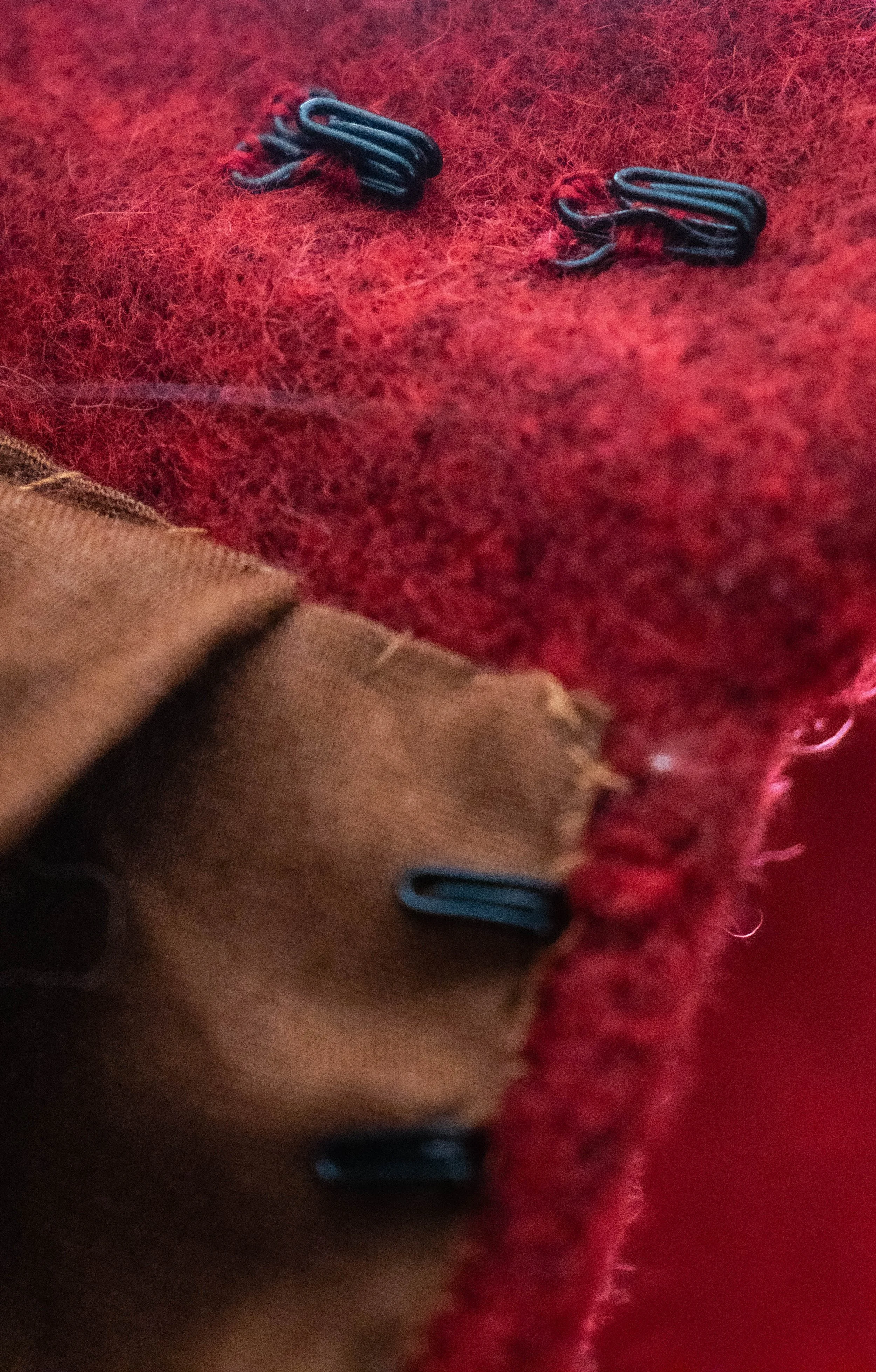 Deux épingles de sécurité noires fixées sur un vêtement rouge avec une texture de tissu laineux.