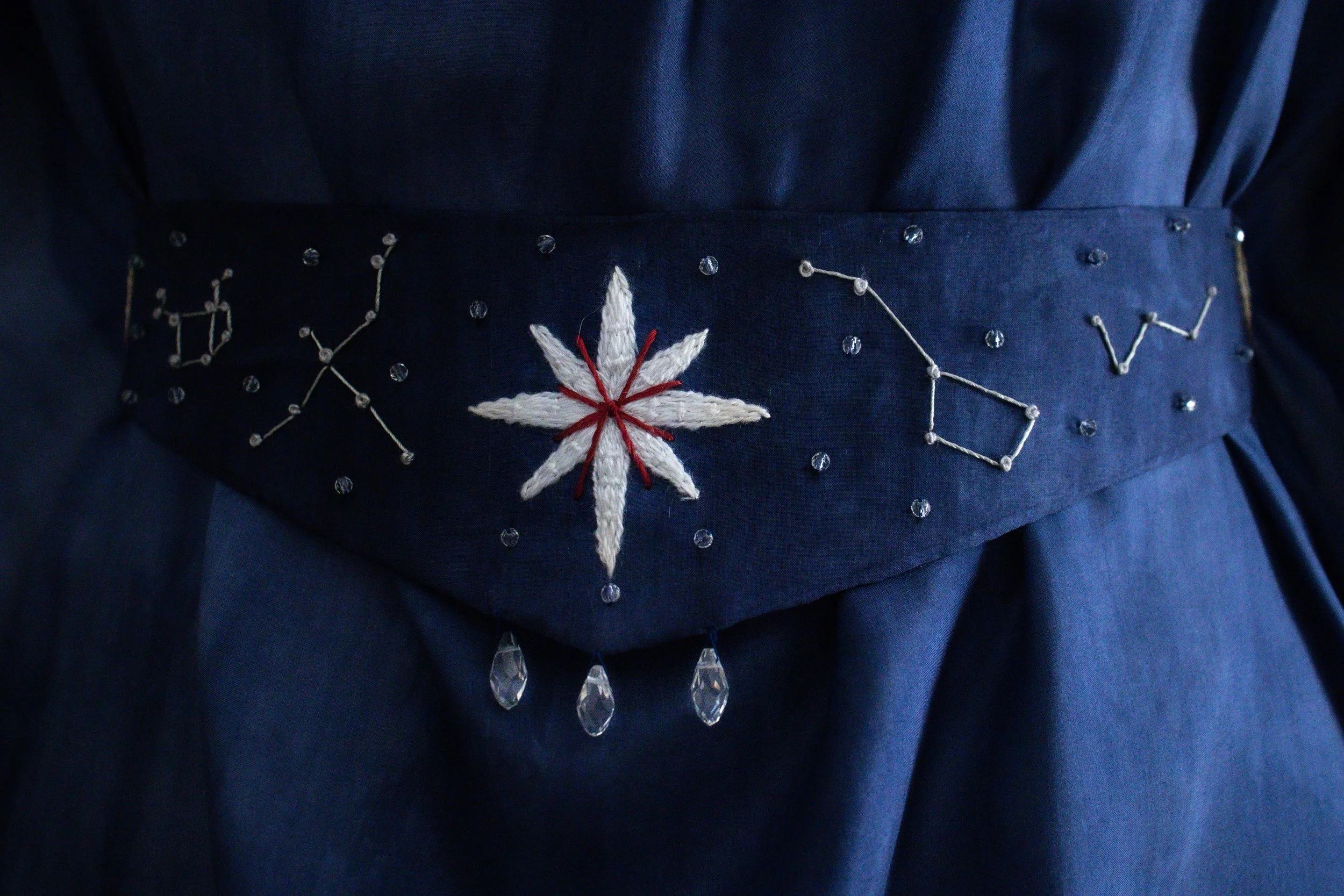 Ceinture noire en tissu de couleur bleu foncé décorée d'un motif en forme de fleur blanche et rouges, avec des petites pierres transparentes cousues autour du motif.