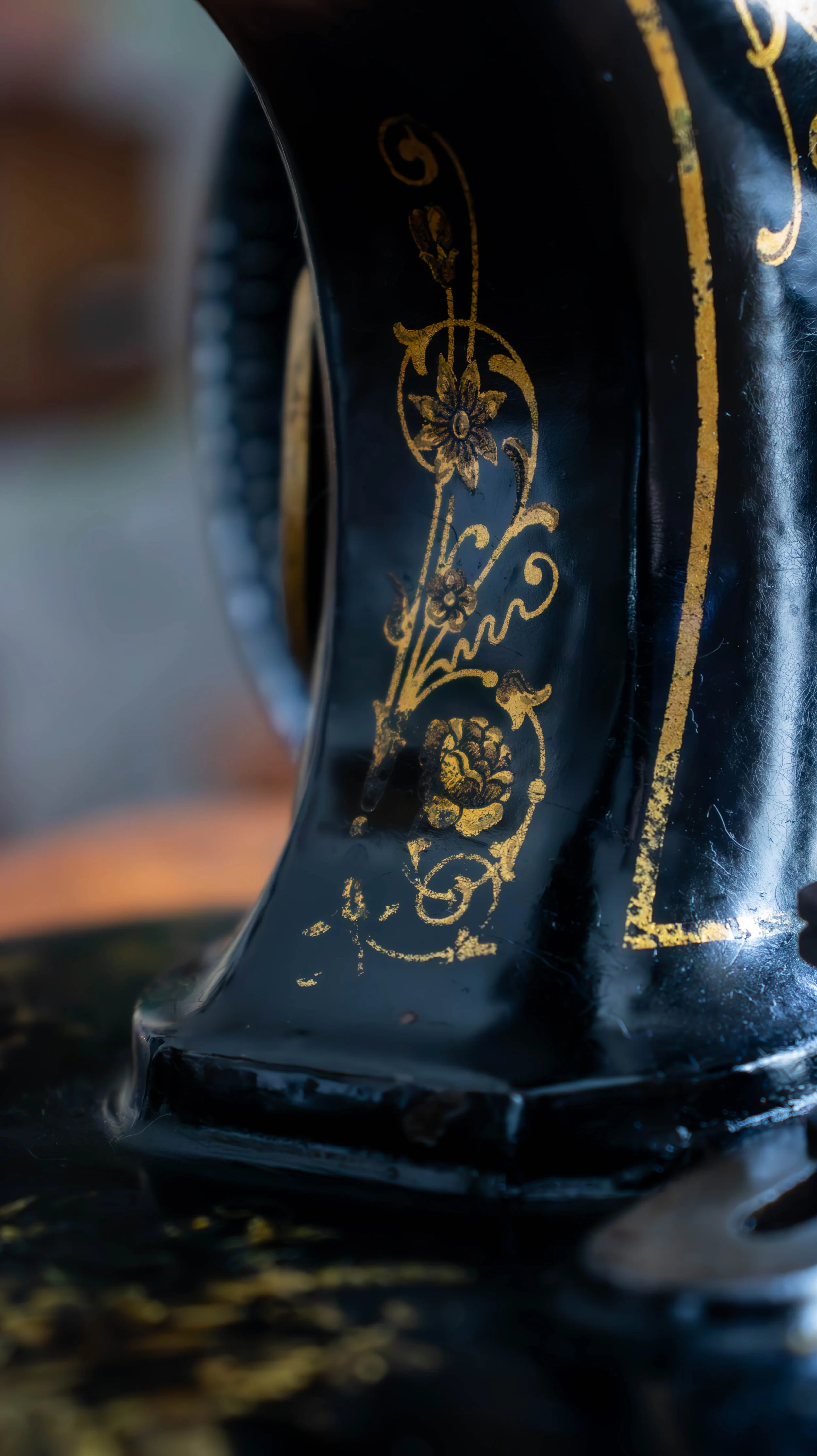 Détail d'une décoration ornementale dorée sur une surface noire, possiblement une pièce d'art ou un objet décoratif en métal ou en céramique.