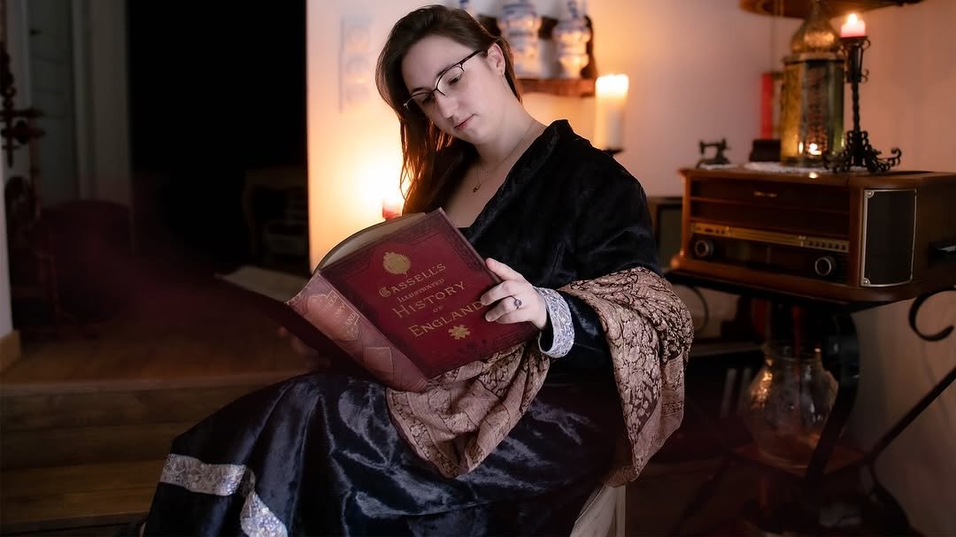 Femme lisant un livre intitulé 'Aseulls Museum: A History of England' dans une pièce chaleureuse et bien décorée.